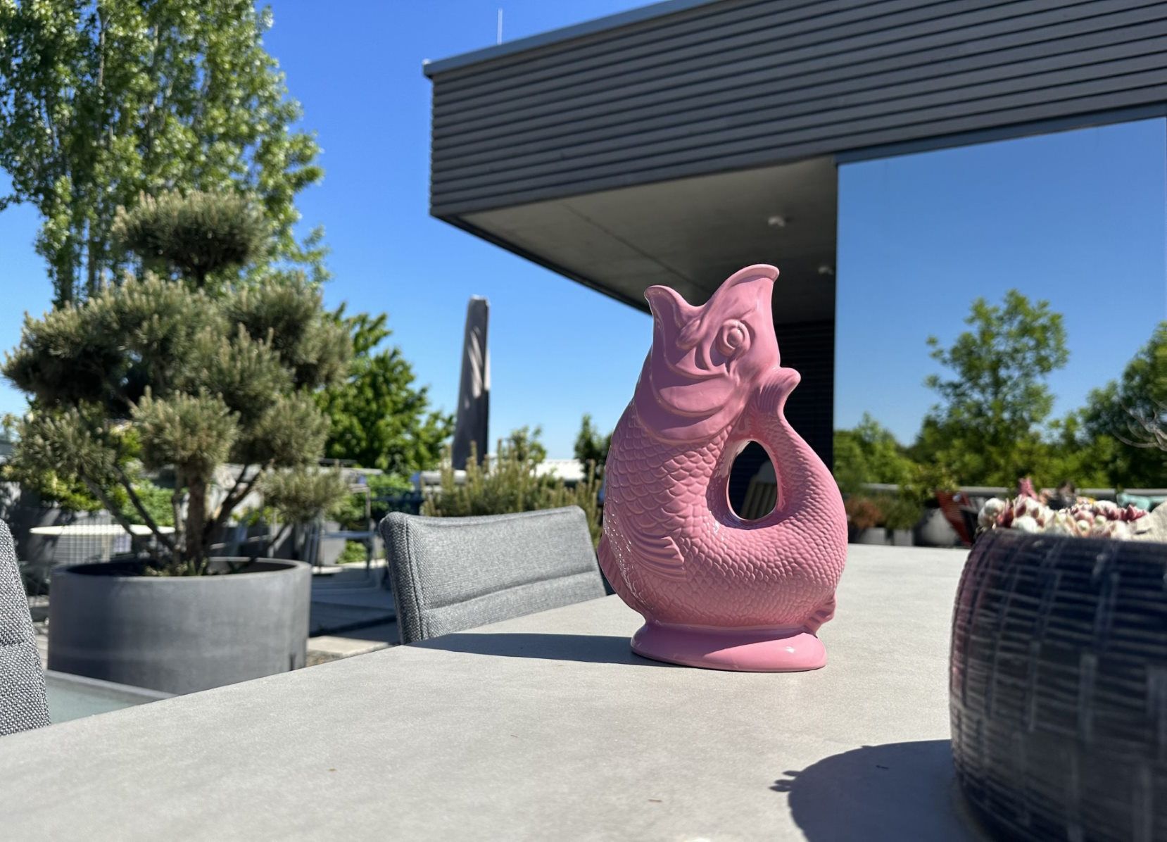 Rosa Gluckigluck Karaffe in Fischform auf einem Tisch im Freien, Dekoration und Vase.