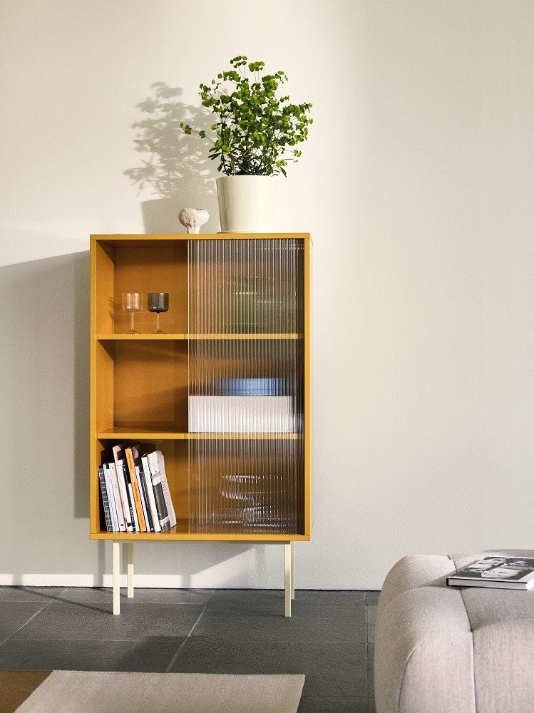 Gelber Hay Colour Cabinet Schrank mit geriffelter Glastür, Büchern, Gläsern und Pflanze im modernen Wohnzimmer.