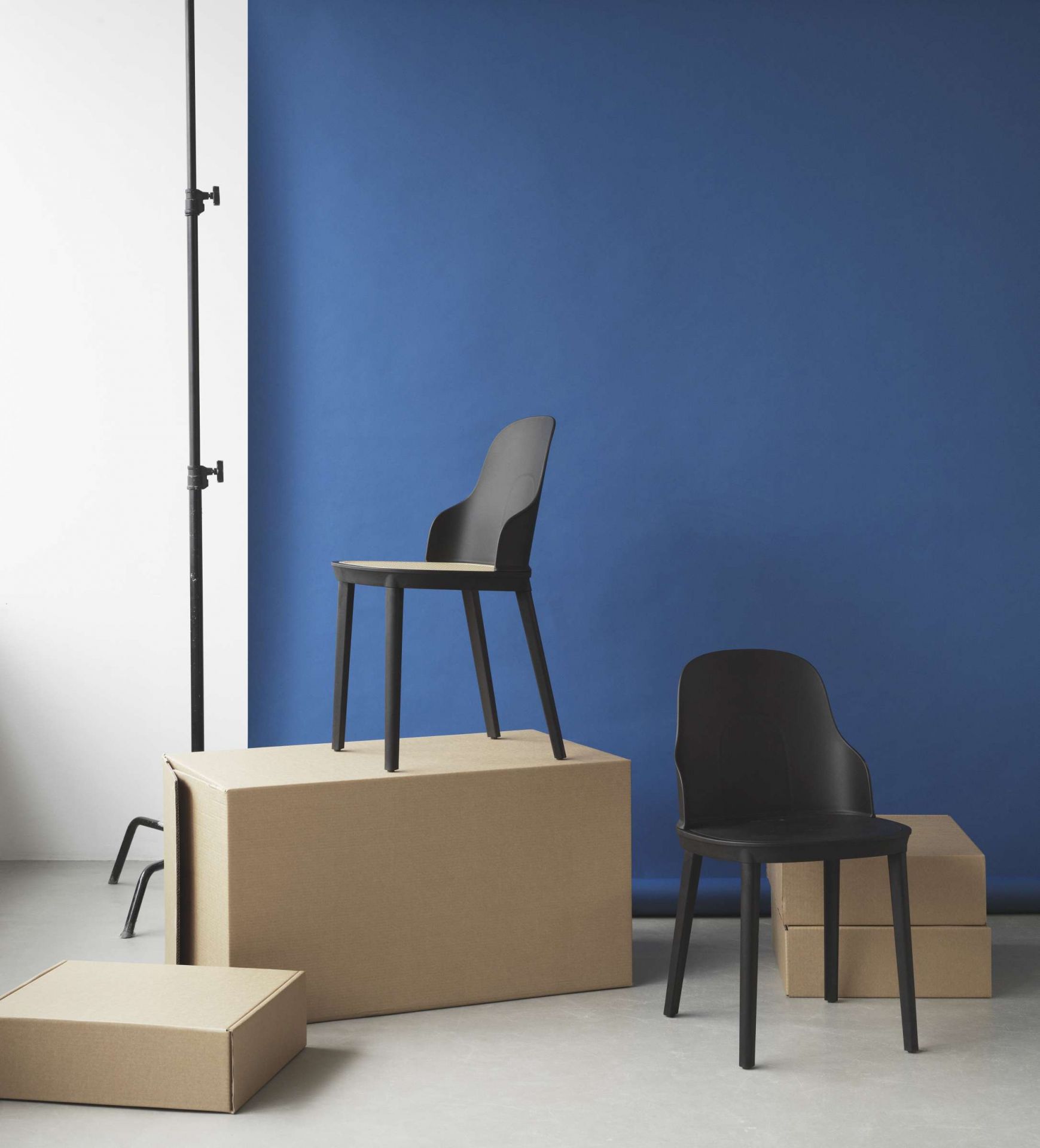 Zwei schwarze Allez Chair Stühle von Normann Copenhagen vor blauem Hintergrund und Kartons.