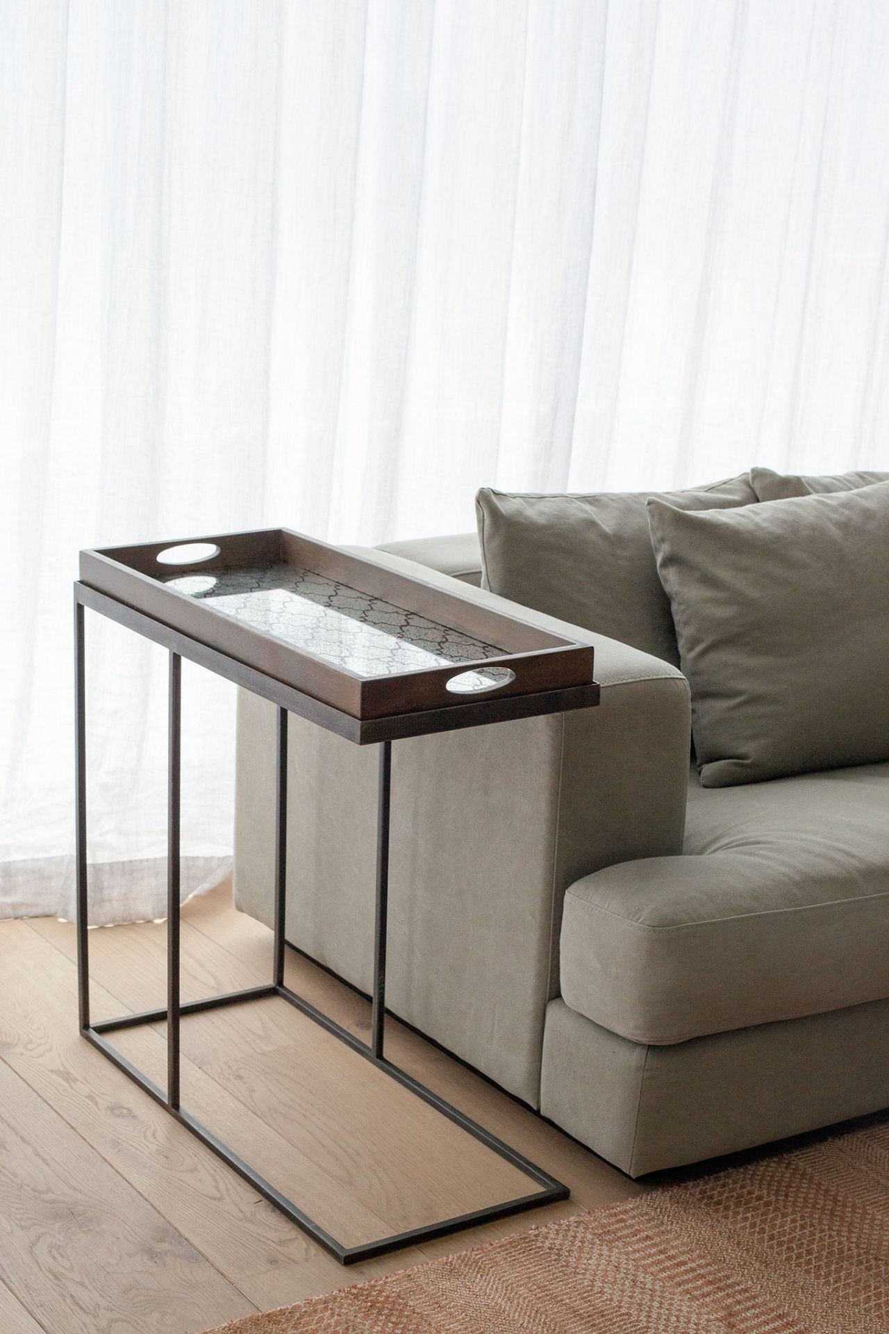 Ethnicraft Beistelltisch aus Holz, schwarz lackiert, neben einem Sofa mit hellen Vorhängen im Hintergrund.