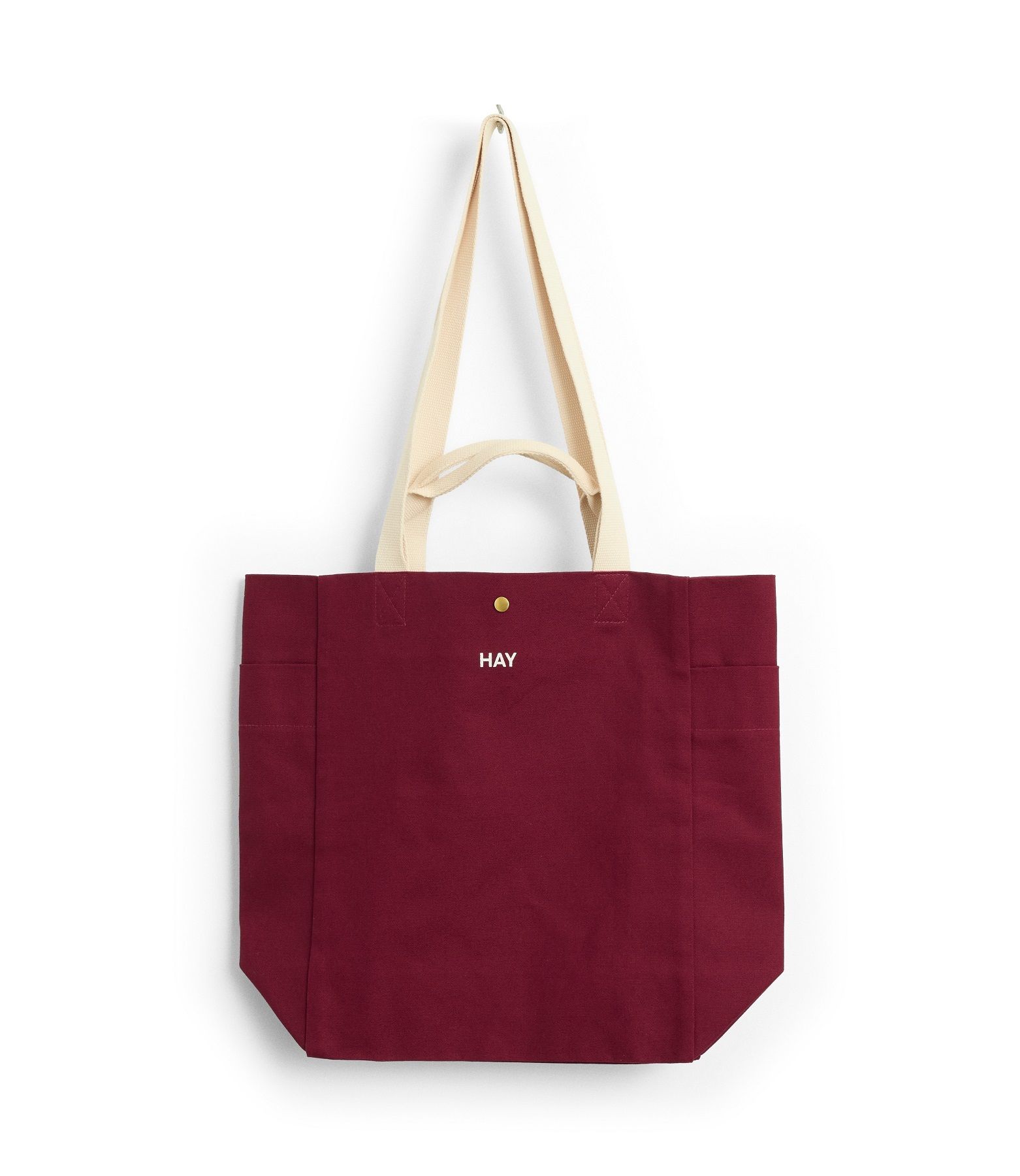 Burgunderrote Hay Everyday Tote Bag aus Baumwolle mit beigen Henkeln, hängend an einer Wand.