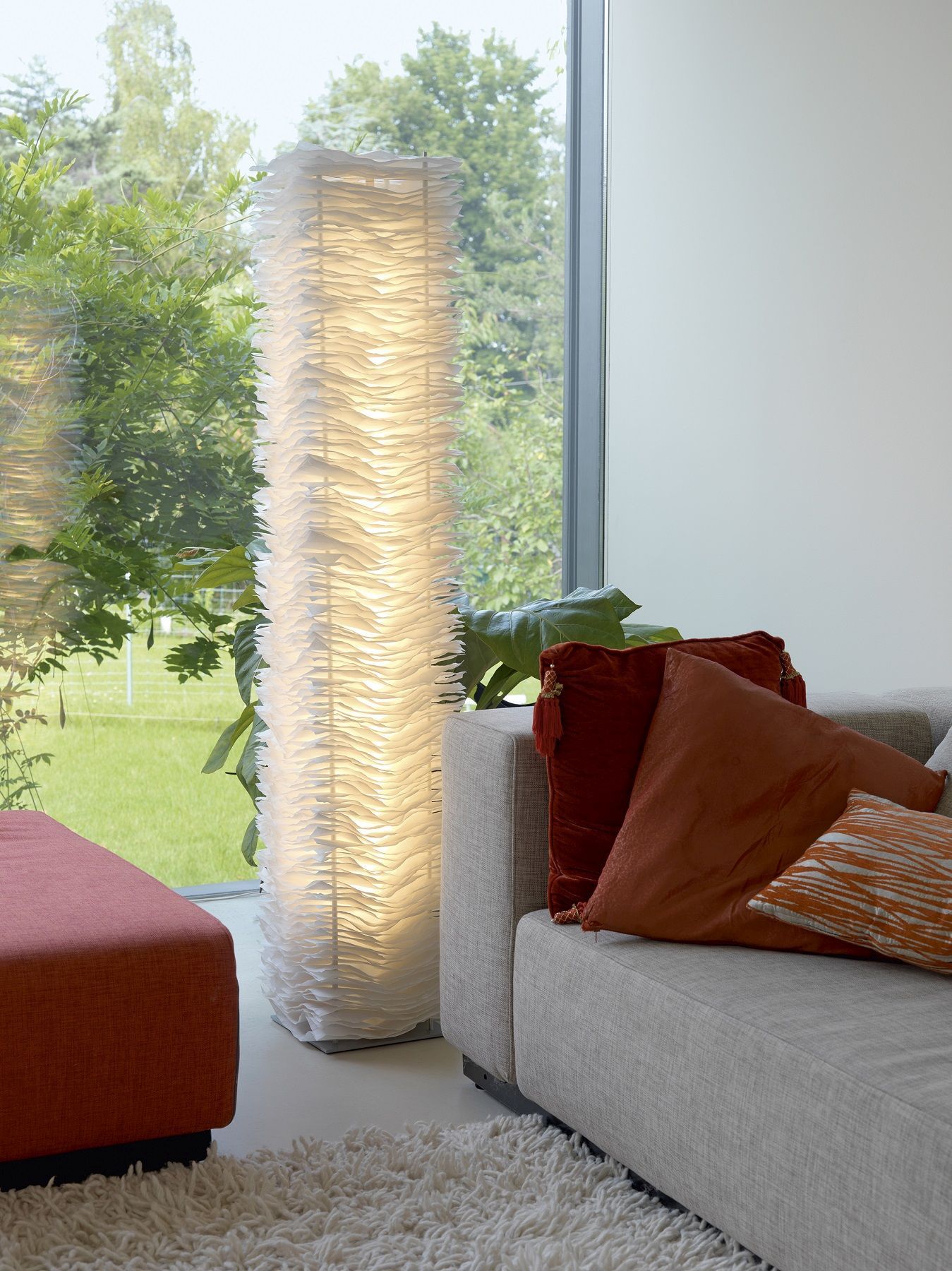 Moderne Stehlampe mit weißem Lampenschirm im Wohnzimmer neben Sofa und Fenster für gemütliche Beleuchtung.