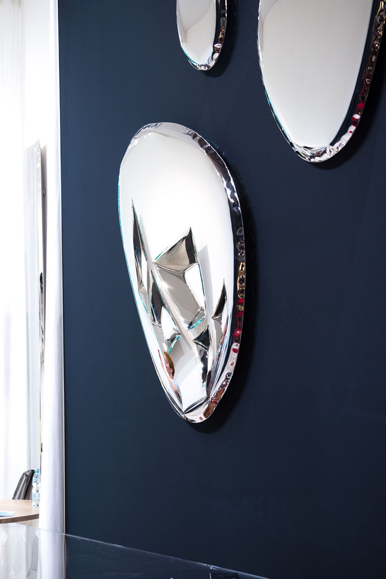 Tafla Spiegel von Zieta, ein moderner Design Wandspiegel mit polierter Oberfläche an einer blauen Wand.