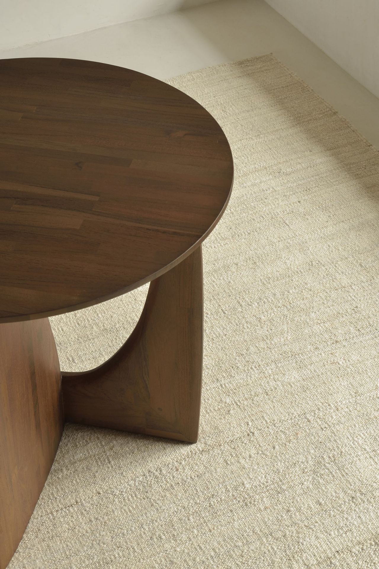 Detailaufnahme: Sandfarbener Ethnicraft Kilim Teppich neben einem runden Holztisch. Hochwertiger, gewebter Teppich.