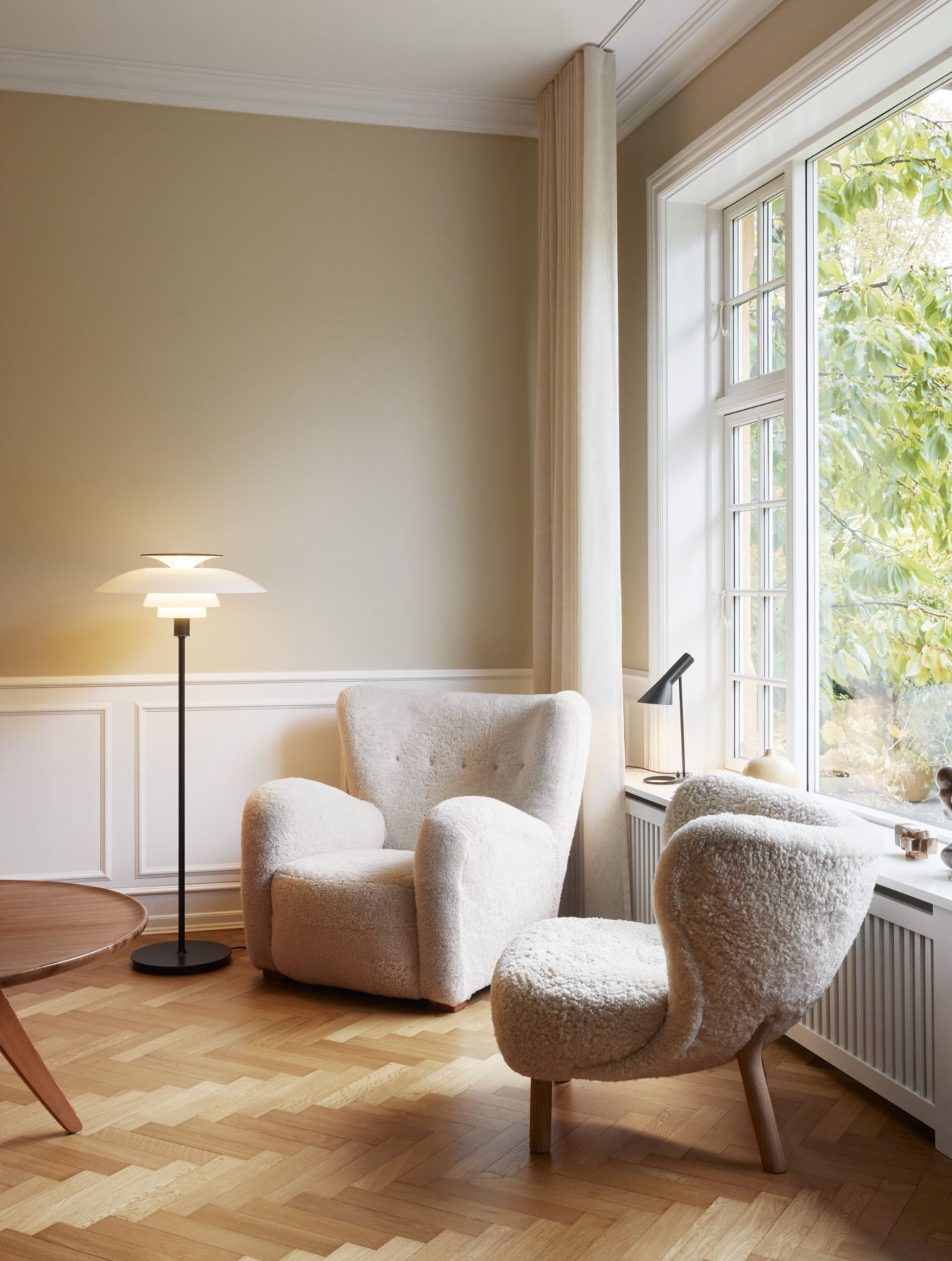 Helles Wohnzimmer mit zwei weißen Sesseln, Stehlampe und Fenster mit Blick ins Grüne.