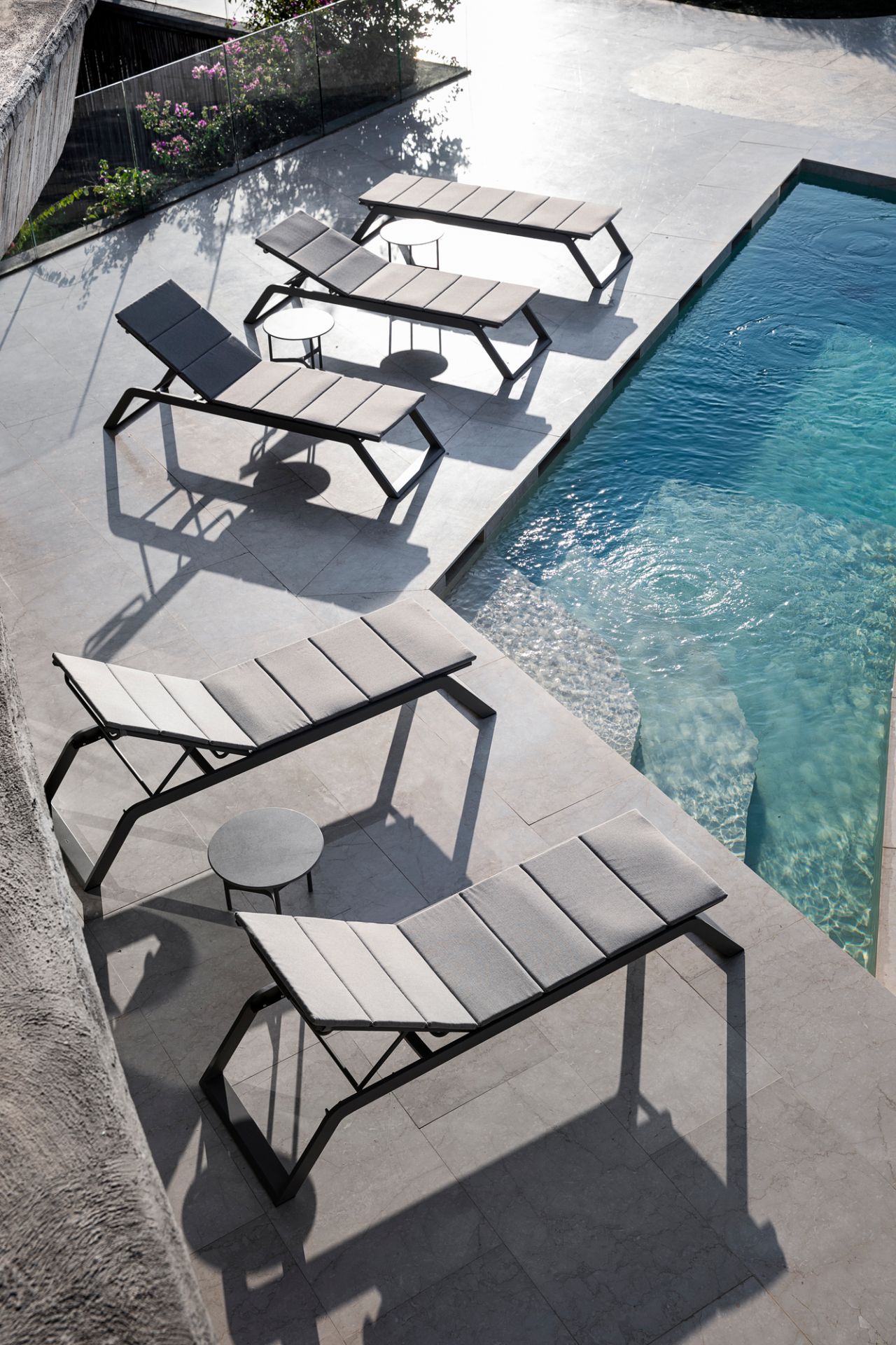 Mehrere Cane-Line Sonnenliegen mit grauen Siesta Outdoor Kissen am Pool. Gartenmöbel für entspannte Stunden.
