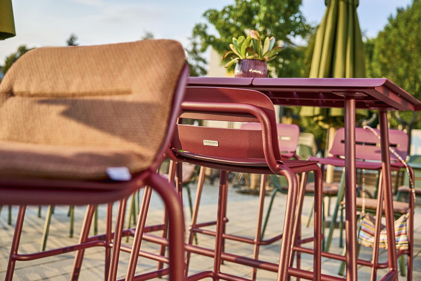 Nahaufnahme des Vapio Hochtisch Outdoor von Weishäupl mit Barhockern in Rot, ideal für Garten und Terrasse.
