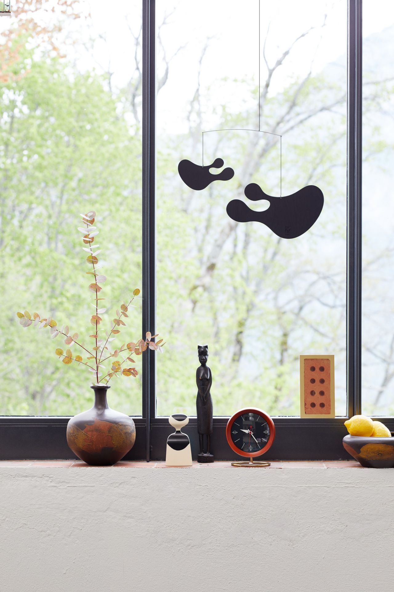 Vitra Chronopak Tischuhr in Orange auf Fensterbank mit Dekoration und Blick ins Grüne.
