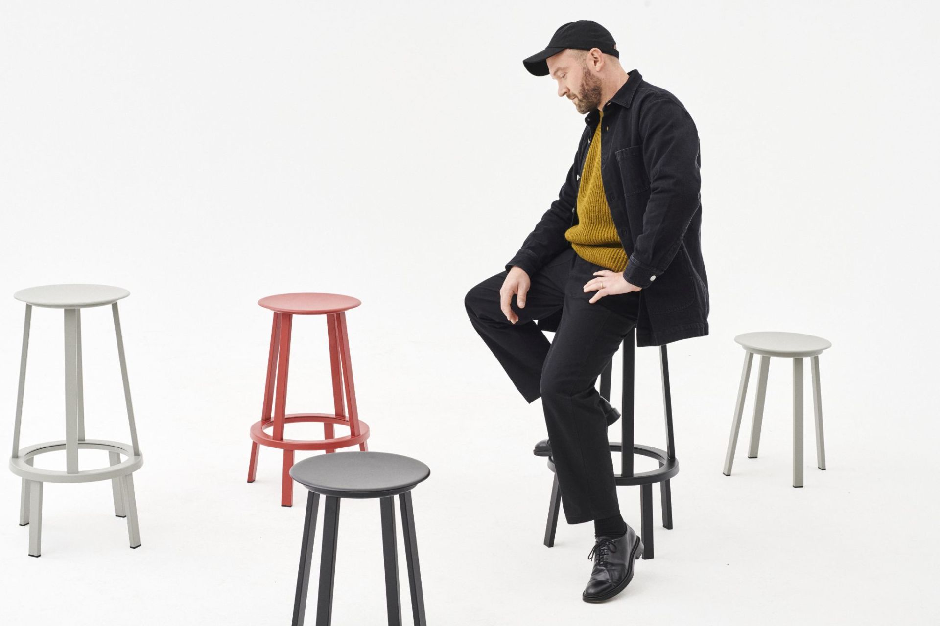 Mann sitzt auf schwarzem Revolver Bar Stool Barhocker High Hay, weitere Hocker in Grau, Rot und Schwarz.