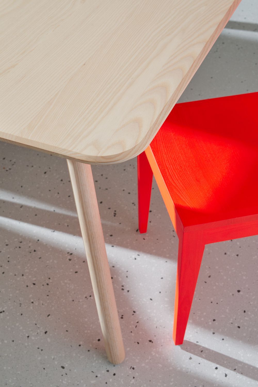 Detailaufnahme des MEYER Tisch Large OUT mit heller Holzplatte und einem roten Stuhl.