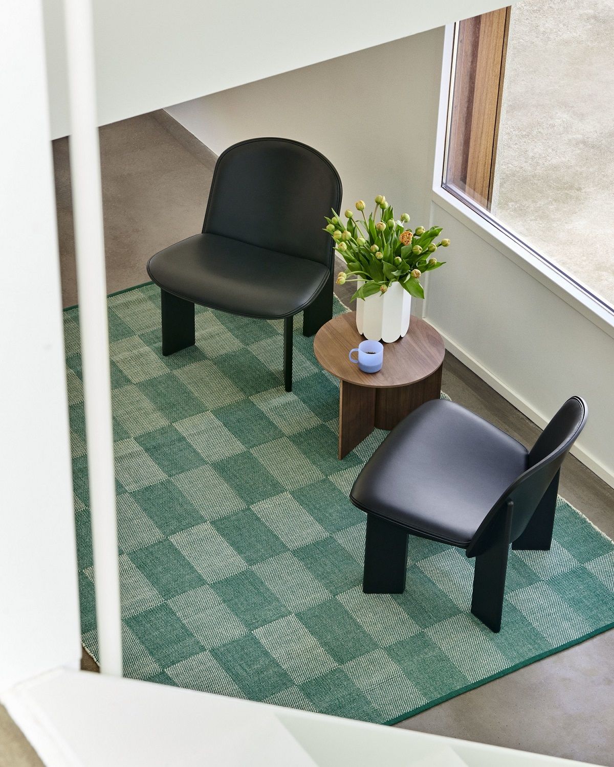 Zwei schwarze Chisel Lounge Sessel von Hay auf einem grün-weiß karierten Teppich, minimalistisches Design.