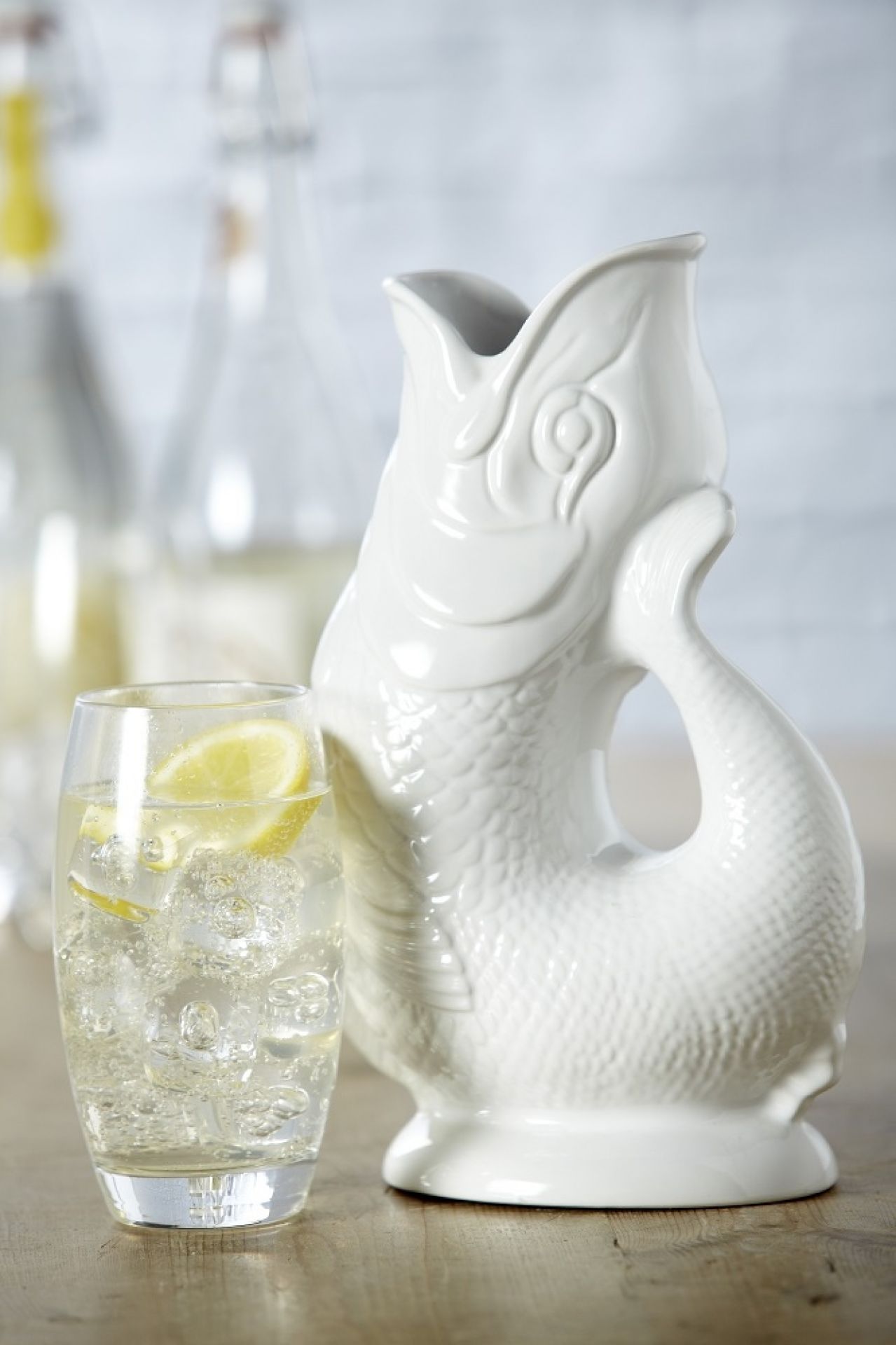 Weiße Gluckigluck Karaffe in Fischform neben einem Glas mit Zitronenwasser. Keramik Wasserkaraffe.