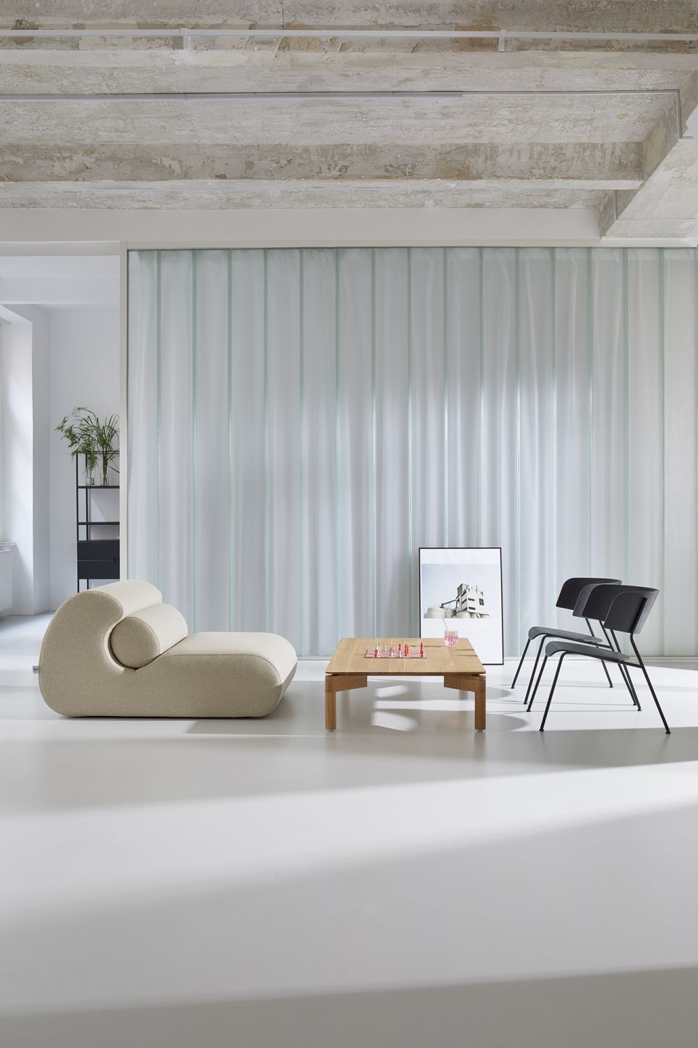 Helles Wohnzimmer mit beigem OLA Sofa Pouf, Holztisch mit Schachbrett und zwei schwarzen Stühlen.