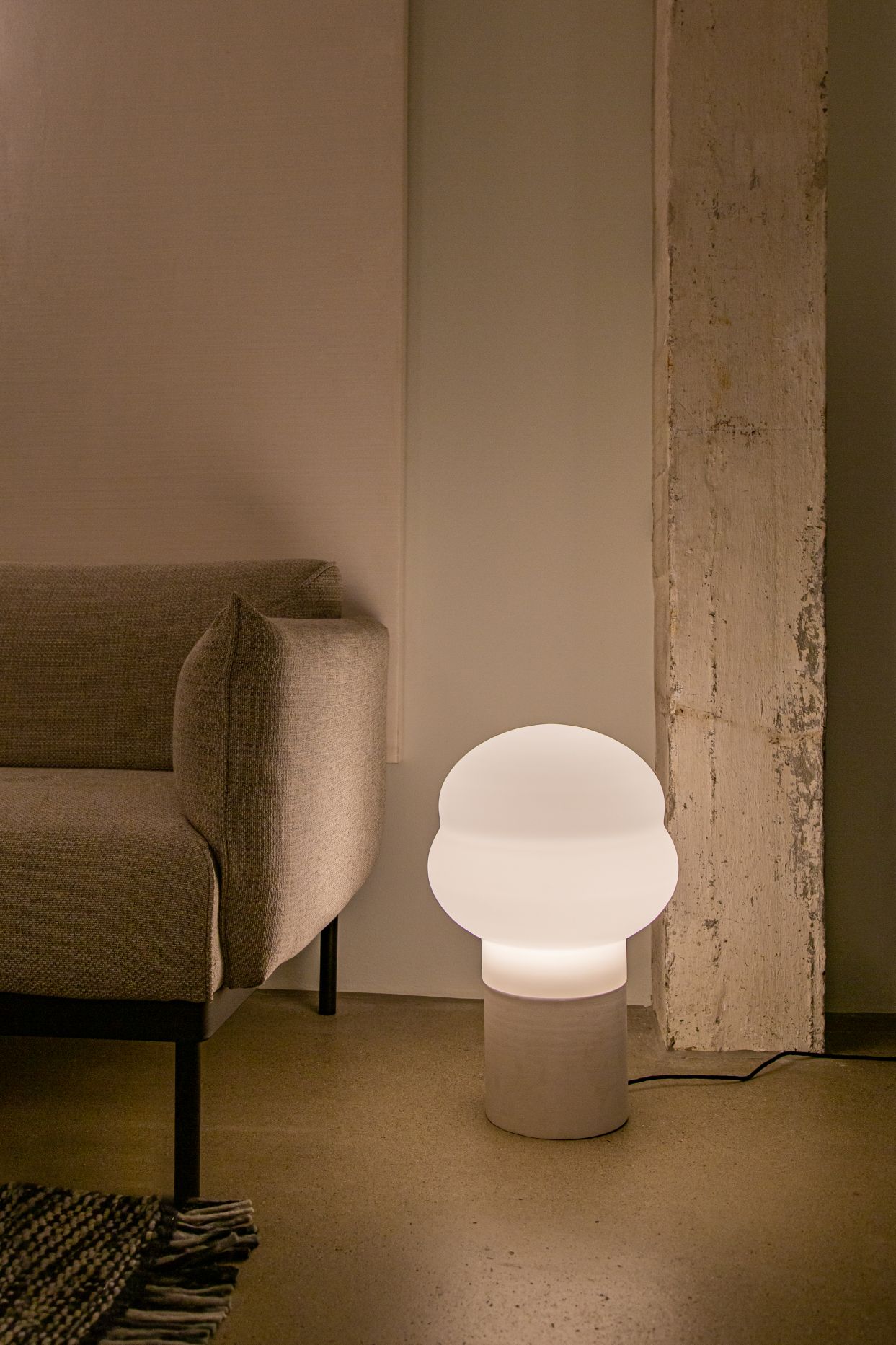 Weiße Kumo Tischleuchte von Pulpo neben einem Sofa, modernes Design für Wohnzimmer.
