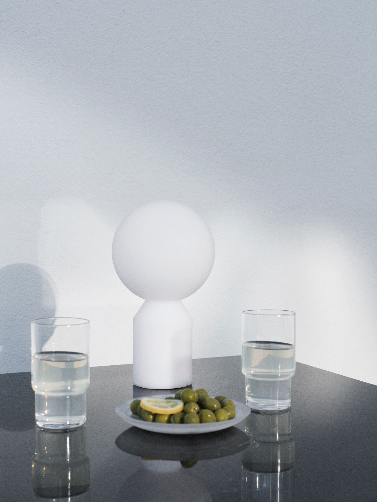 Nahaufnahme der Normann Copenhagen Yo Lamp Tischleuchte, mit Oliven und Getränken auf einem Tisch.