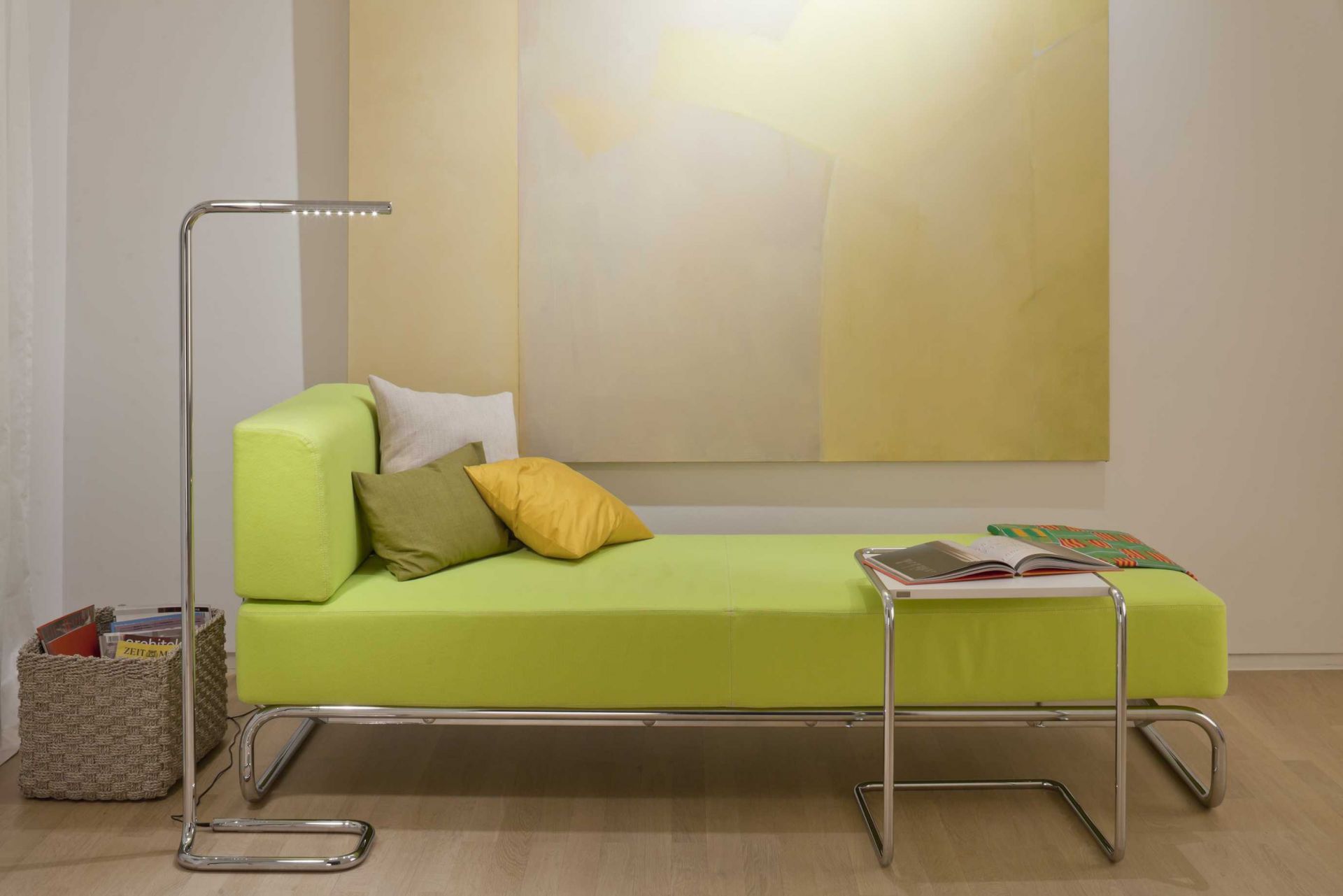 Lum LED Stehleuchte von Thonet, verchromt, neben grüner Liege mit Kissen im Wohnzimmer.