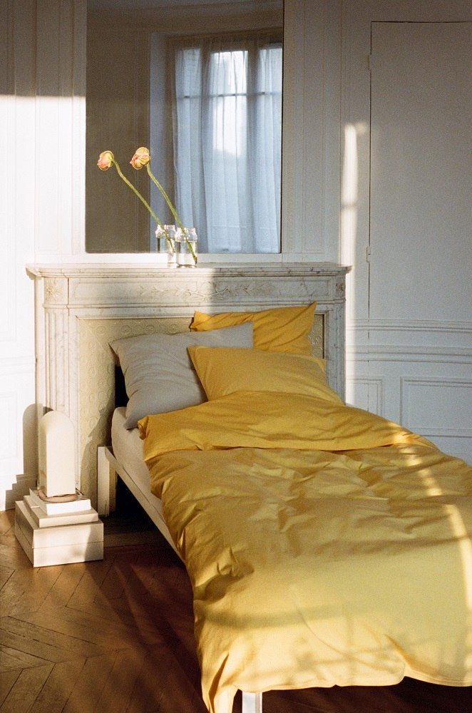 Helles Schlafzimmer mit Hay Connect Bett, gelber Bettwäsche, Kissen und Blumen auf dem Kaminsims.