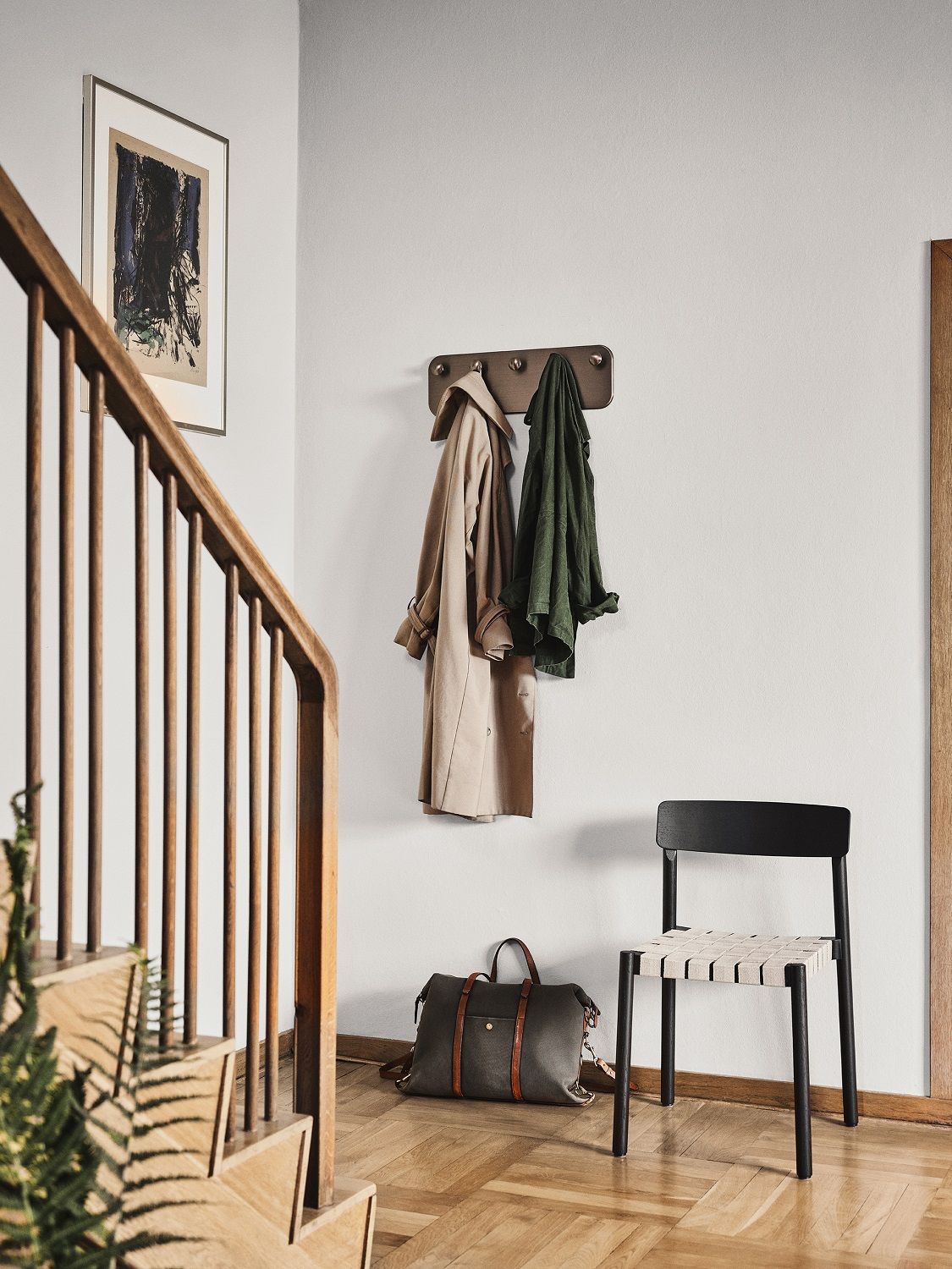 AndTradition Betty TK1 Stuhl im Flur mit Kleiderhaken, Tasche und Holztreppe. Schwarzer Holzstuhl mit Stoffbespannung.