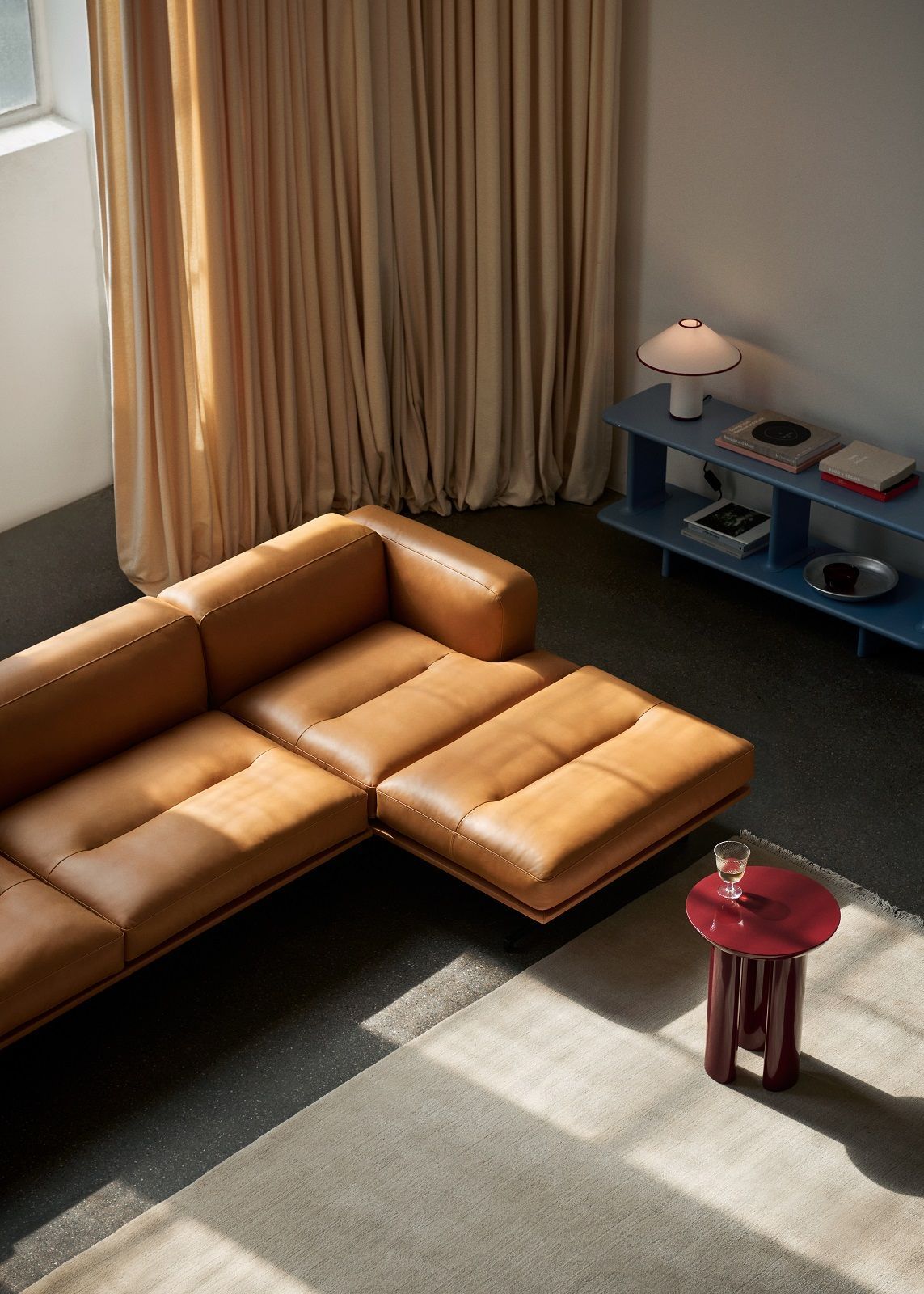 AndTradition Inland AV41 Ledersofa in hellem Braun, kombiniert mit rotem Beistelltisch und blauem Regal.