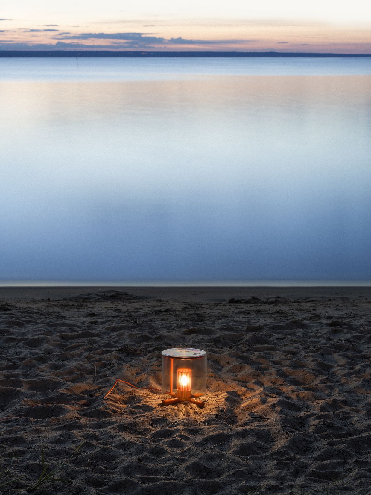Fireplace Lamp Tischleuchte von Design House Stockholm auf Sandstrand mit Meer im Hintergrund.