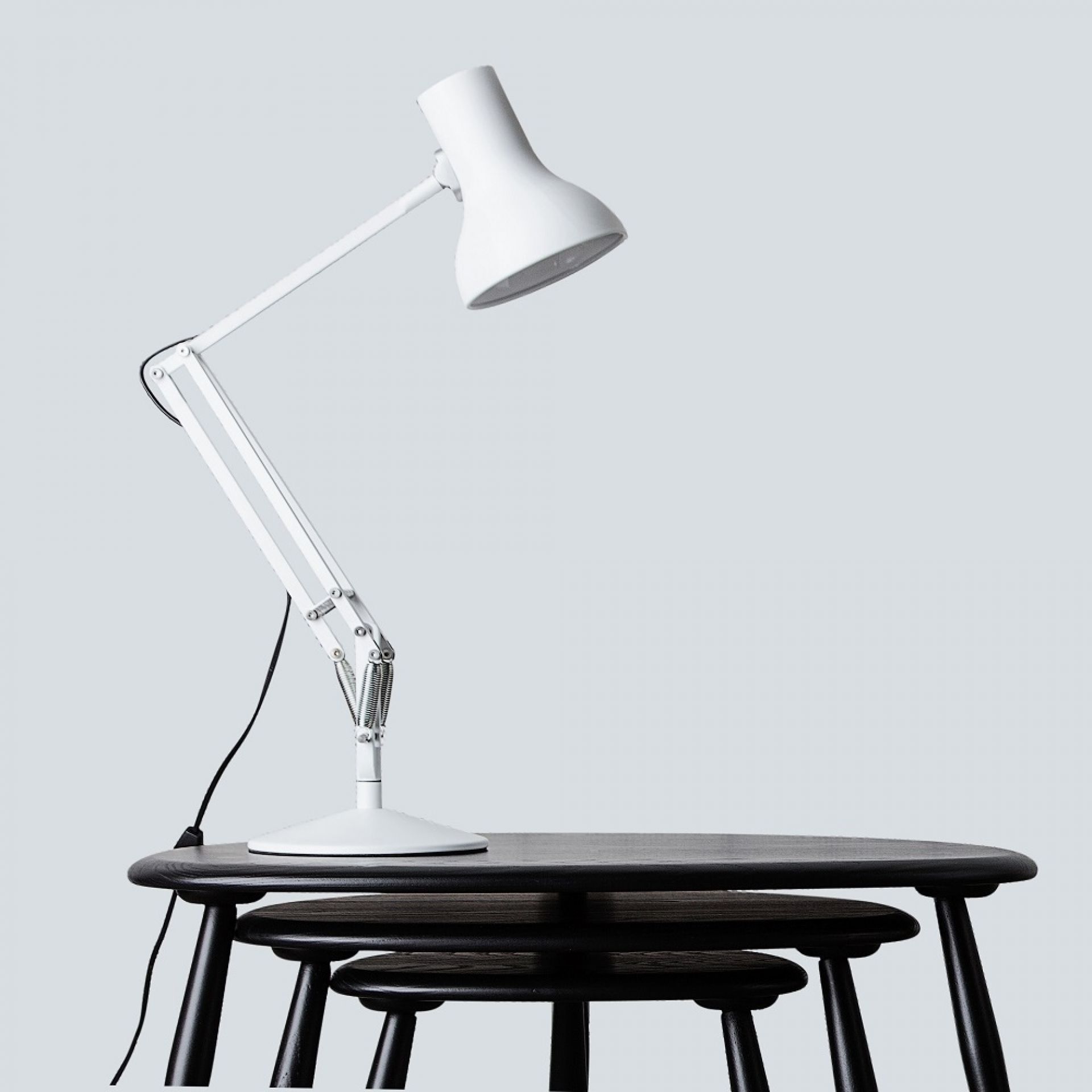 Weiße Anglepoise Type 75 Mini Tischleuchte auf einem schwarzen Holztisch, modernes Design.