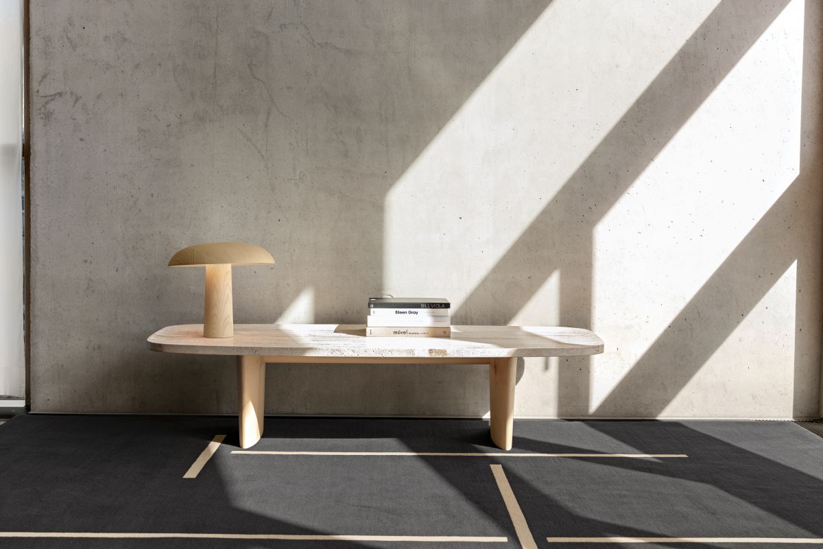 Forma Tischleuchte von ClassiCon aus hellem Holz auf einem Tisch mit Büchern und Teppich.