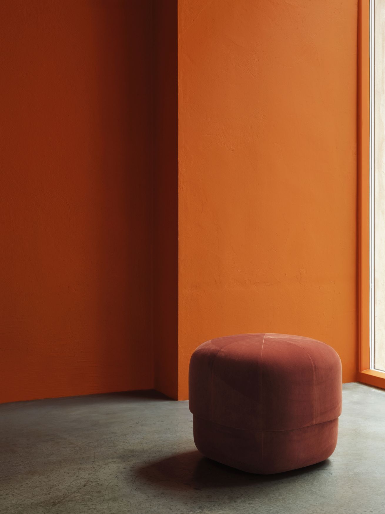 Nahaufnahme des Circus Pouf Small Hockers von Normann Copenhagen in Terrakotta vor orangefarbener Wand.