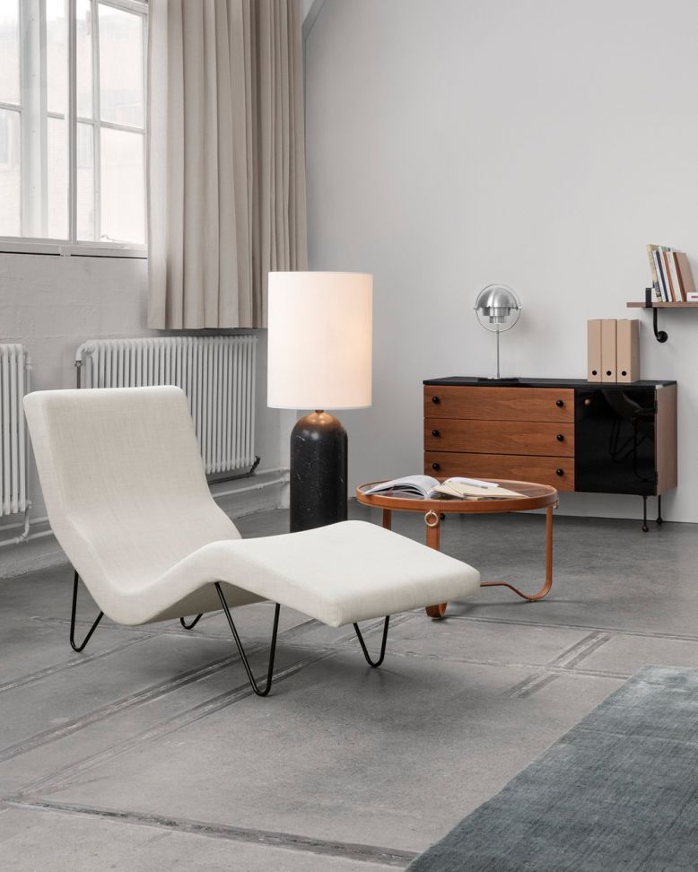 Gubi Multi-Lite Tischleuchte in Schwarz/Messing neben einem Sessel in einem modernem Wohnzimmer.