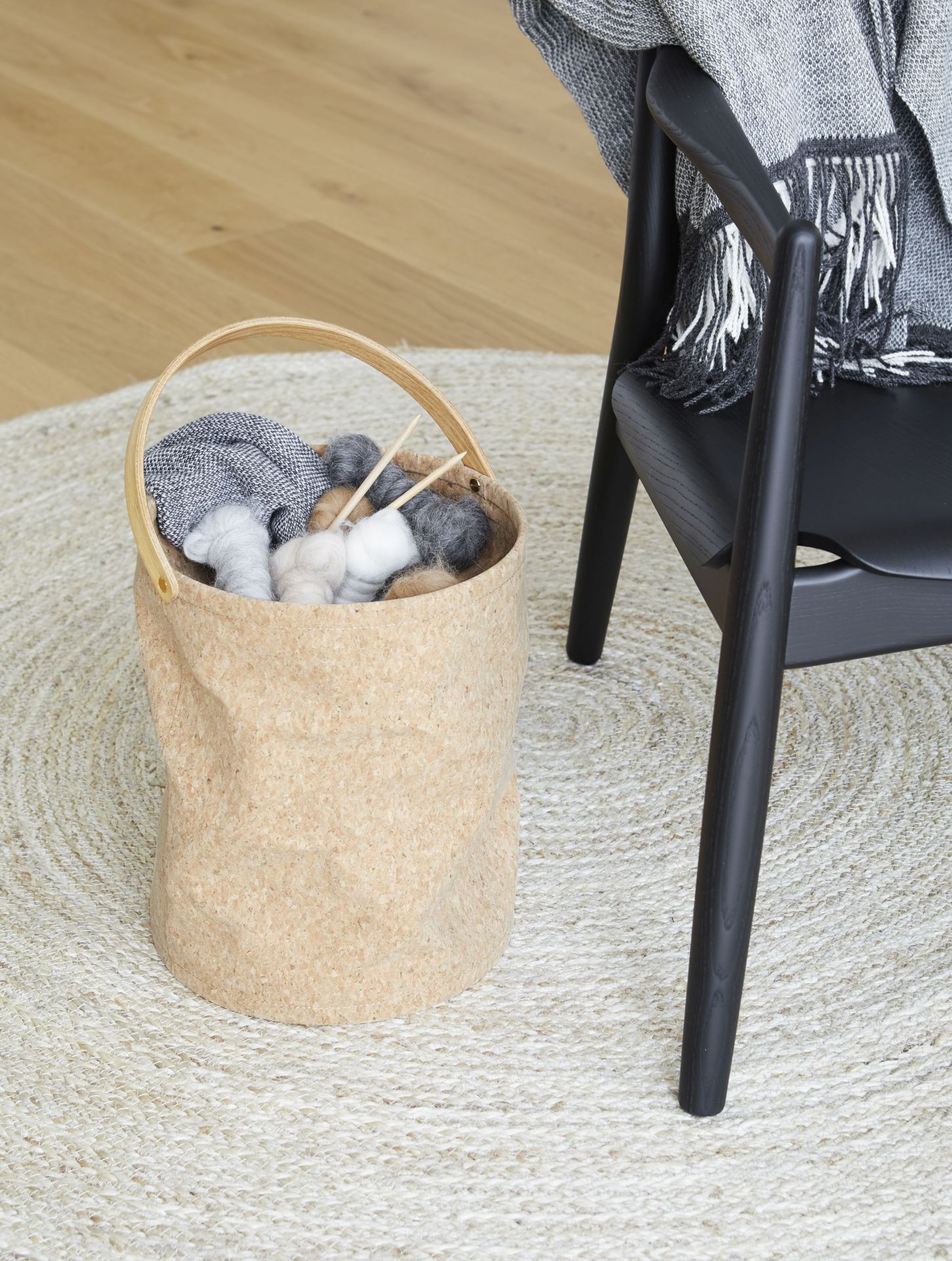 Aymara Decke in Korb neben Stuhl: Weiche Wohndecke, Strickwolle und Stricknadeln im skandinavischen Wohnzimmer.