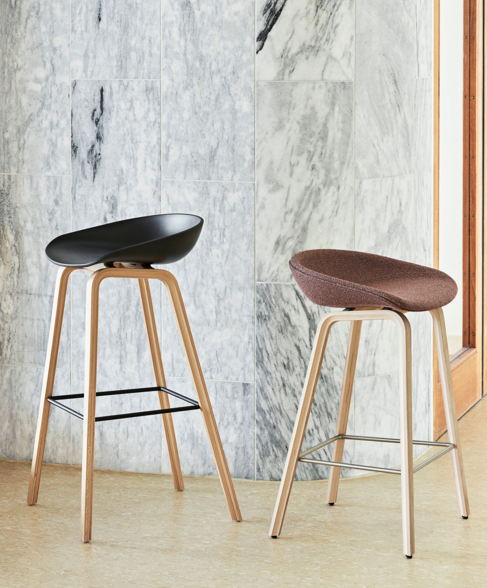 Zwei About a Stool AAS33 Barhocker mit Vollpolsterung in Schwarz und Braun vor Marmorwand.