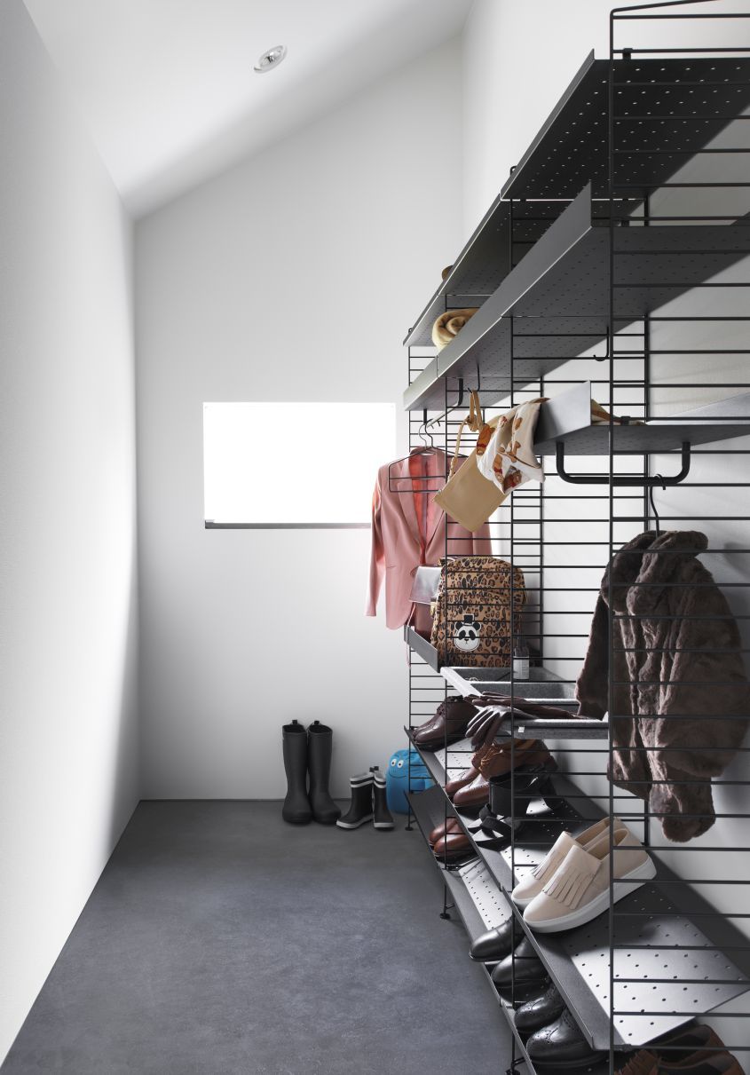 Schwarzes String Regal mit Kleidung, Schuhen und Accessoires, inklusive Kleiderbügeln für Jacken und Taschen.