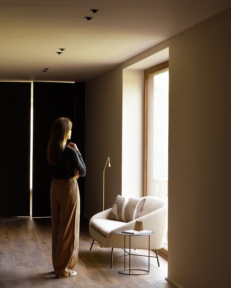 Frau betrachtet Ethnicraft Sessel Barrow in Off-White mit Kissen und Beistelltisch im modernen Wohnzimmer.