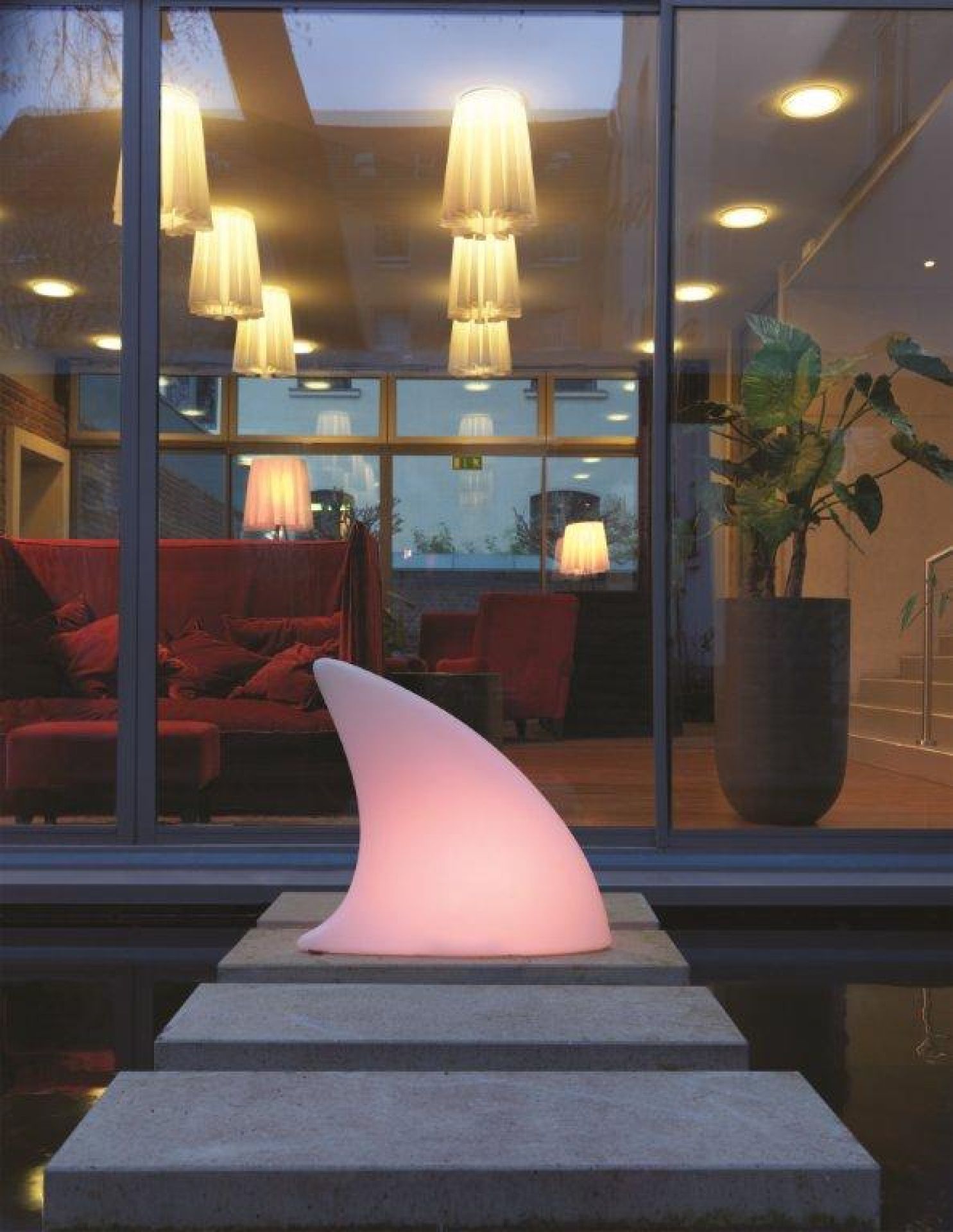 Moree Shark Haifischflosse Bodenleuchte, leuchtend rosa, auf Steinstufen vor einem Fenster mit Spiegelung.