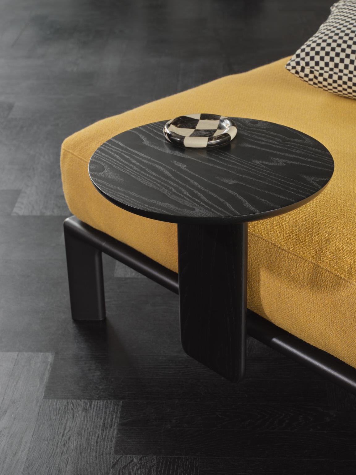 Schwarzer Anagram Anstecktisch von Vitra neben einem gelben Sofa mit Schachbrettmuster-Dekoschale auf der Tischplatte.