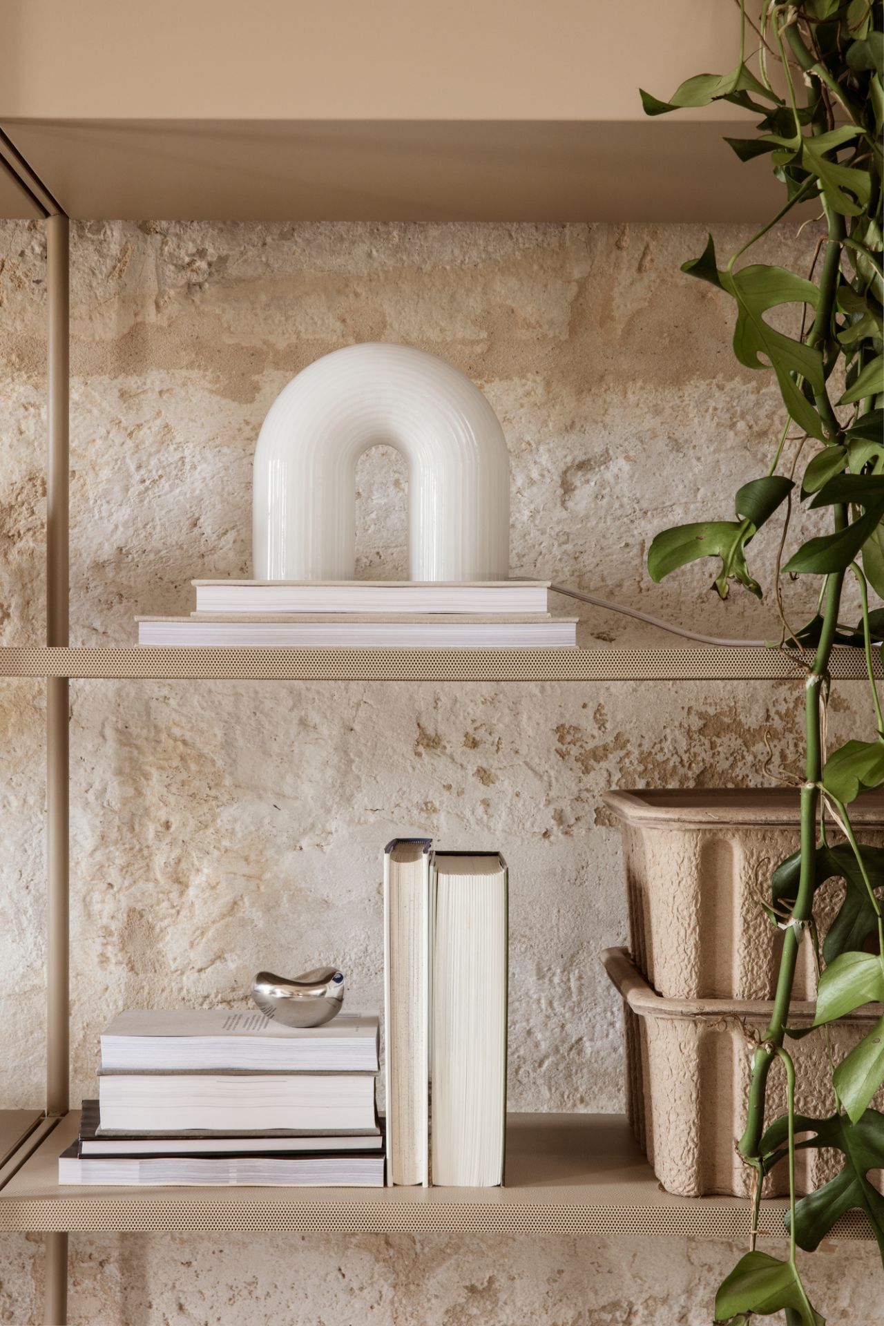 Nahaufnahme der Ferm Living Vuelta Tischleuchte, eine moderne Bogenlampe aus Opalglas, auf einem Bücherregal.