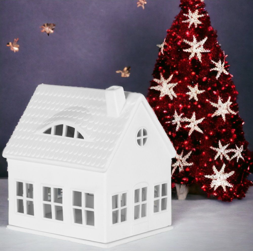 Weißes Räder Lichthaus Gaubenhaus aus Porzellan mit Fenstern und Schornstein, neben rotem Weihnachtsbaum mit Sternen.