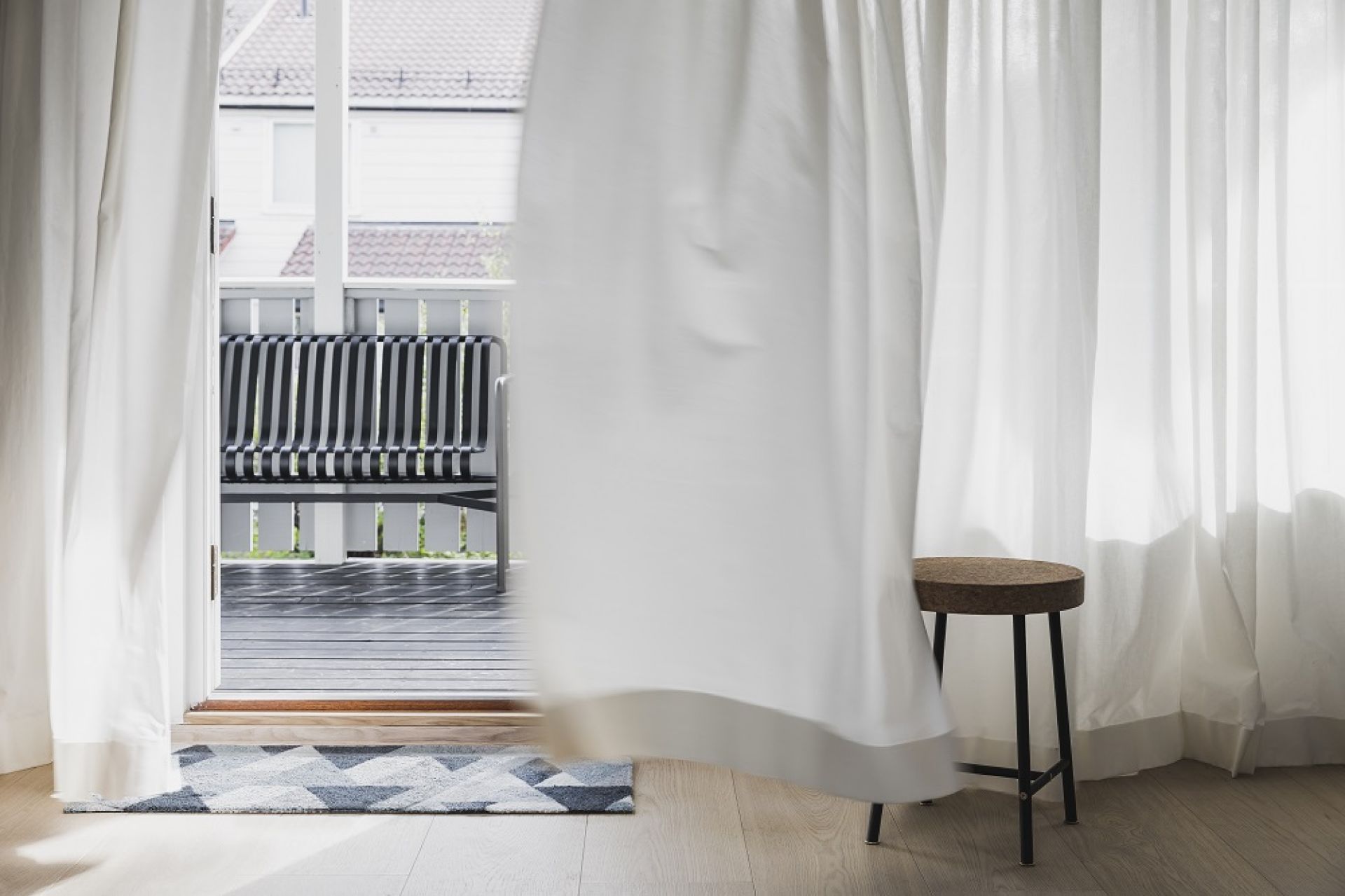 Blåne Heymat Fußmatte im Eingangsbereich mit geometrischem Muster, Blick auf Terrasse mit Bank durch wehende Vorhänge.
