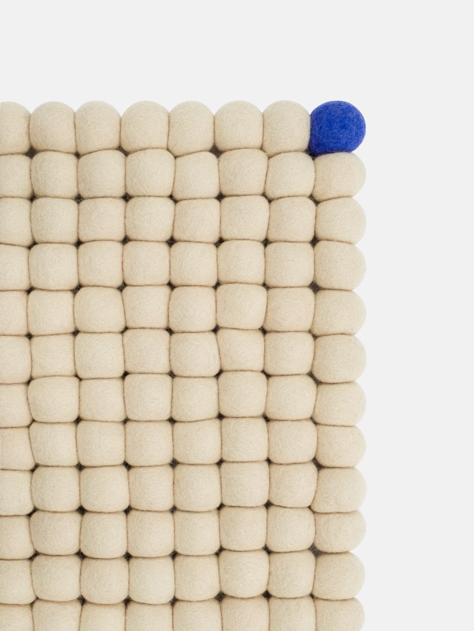 Detailansicht: Beige myfelt Filzteppich "Big One" (180x260 cm) mit blauer Filzkugel. Handgefertigter Wollteppich.