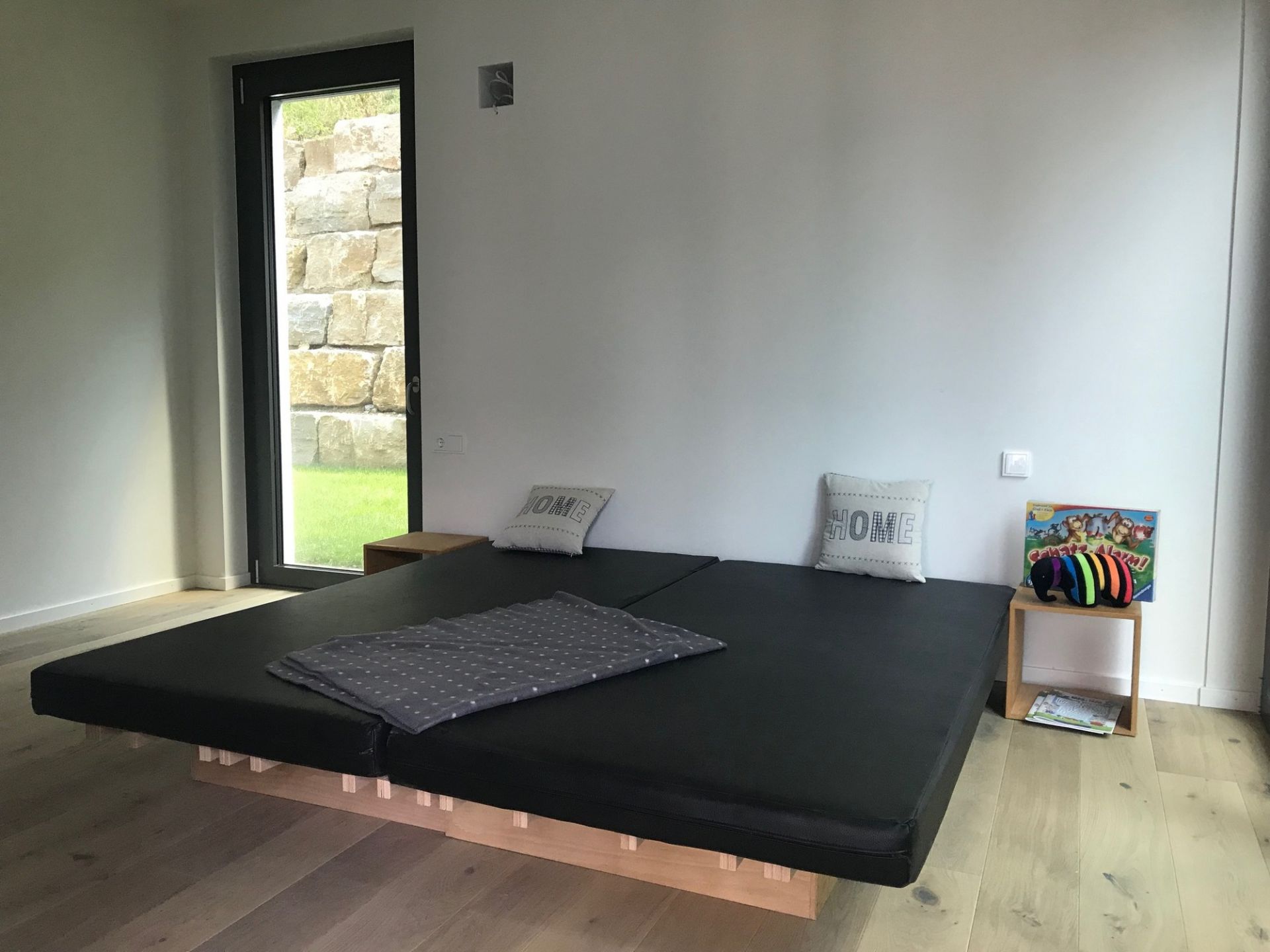 Tojo V Bett 90/180: Modulares, schwarzes Futonbett mit Lattenrost und zwei Kissen im modernen Schlafzimmer.