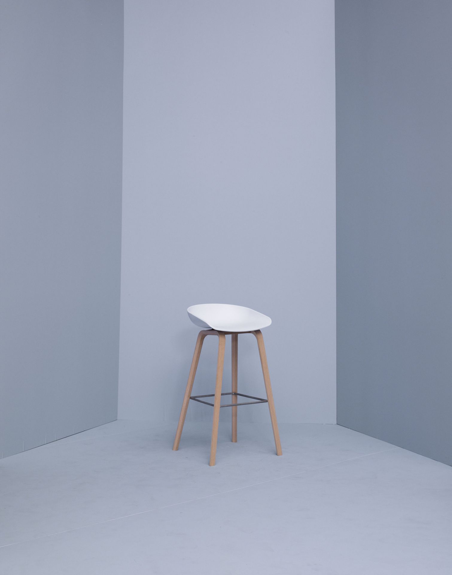 Weißer Hay About a Stool AAS32 Barhocker mit Holzbeinen vor grauem Hintergrund. Moderner skandinavischer Barstuhl.