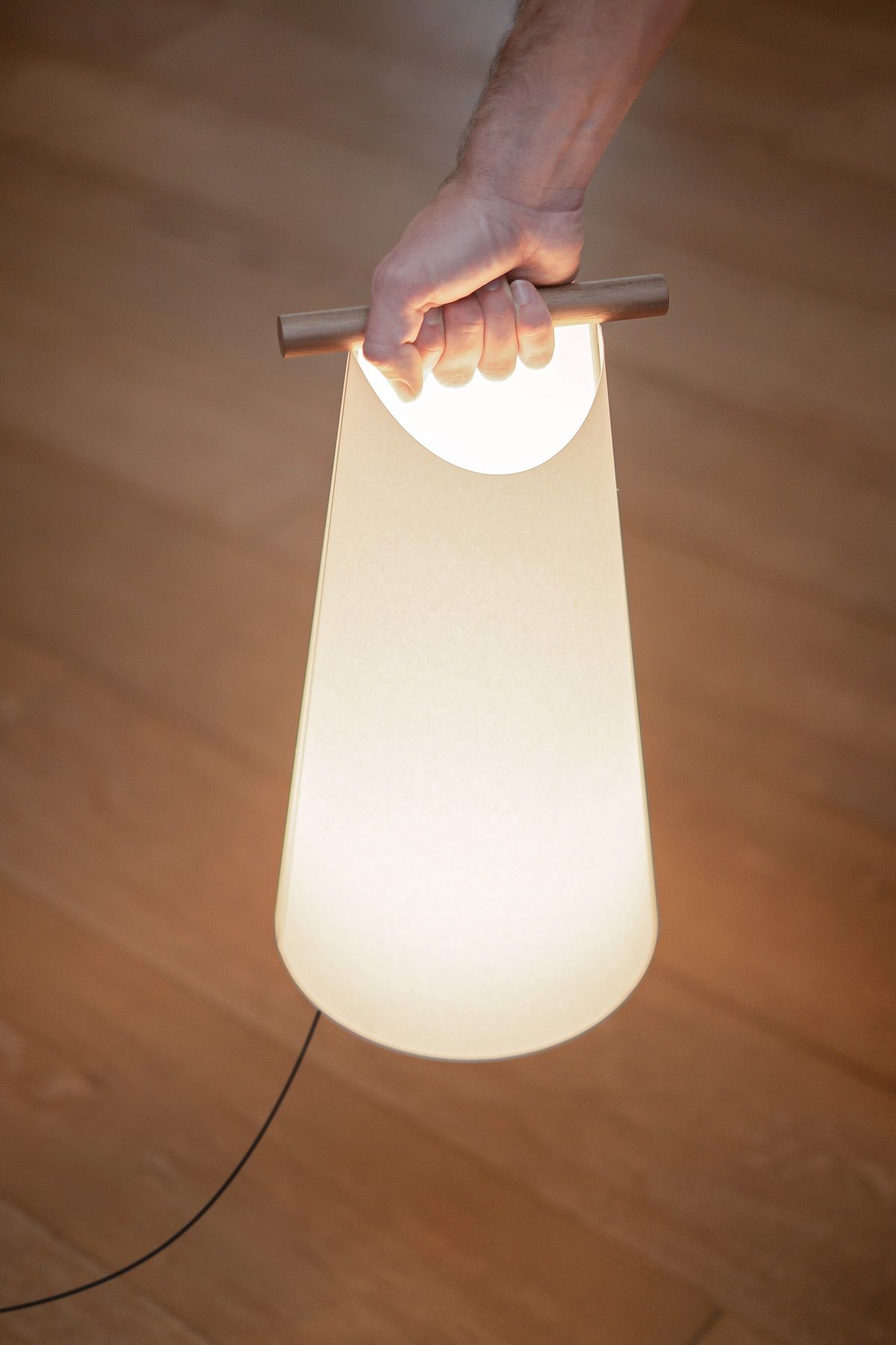 Hand hält leuchtende Catay Tischleuchte von Nomon, moderne Akku-Tischlampe mit Holzgriff.