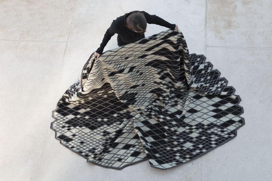 Person drapiert Losanges Teppich von Nanimarquina (230x300 cm) mit geometrischem Muster auf hellem Untergrund.