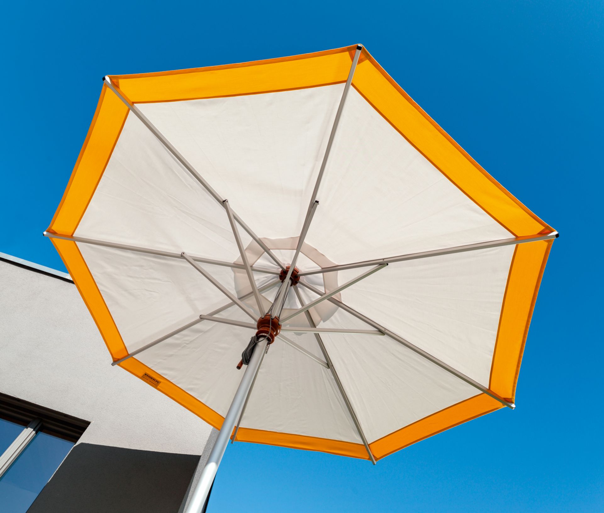 Ansicht von unten: Grauer Weishäupl Sonnenschirm mit Aluminiumgestell und orangefarbenem Rand vor blauem Himmel.