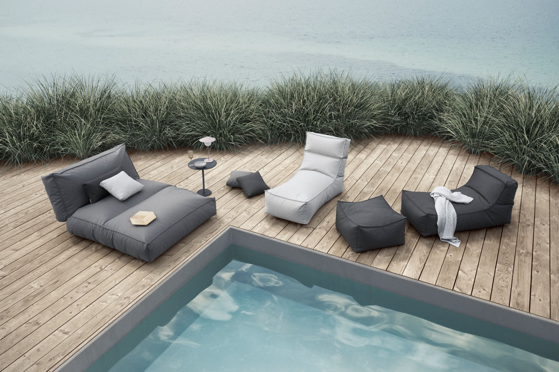 Blomus Stay Outdoor Kissen und Loungemöbel in Grau und Weiß auf Holzterrasse am Pool.