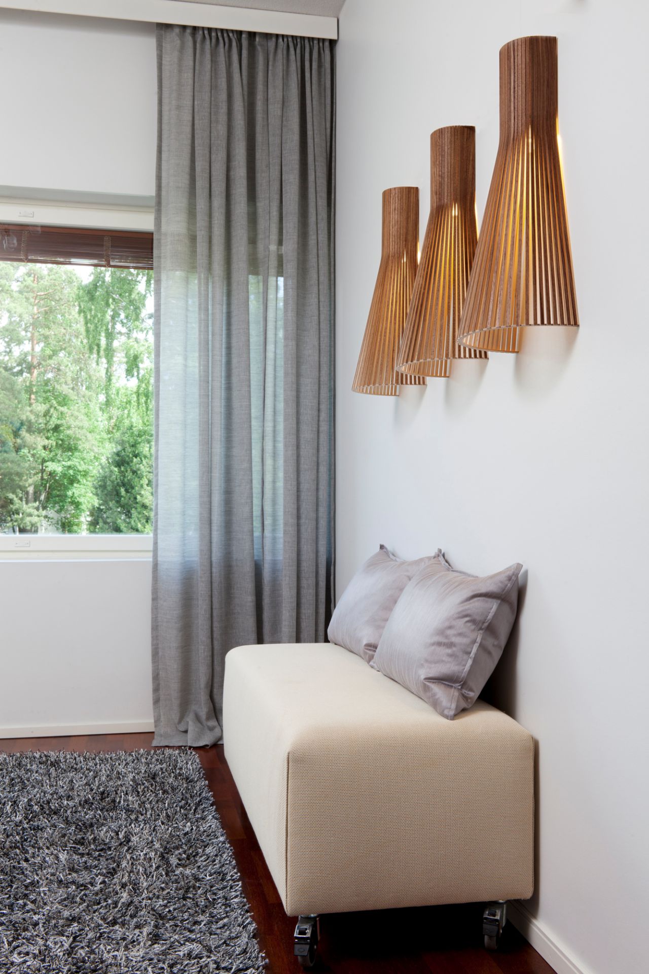 Secto 4230 LED Wandleuchte aus Holz über einer Sitzbank mit Kissen im Wohnzimmer.