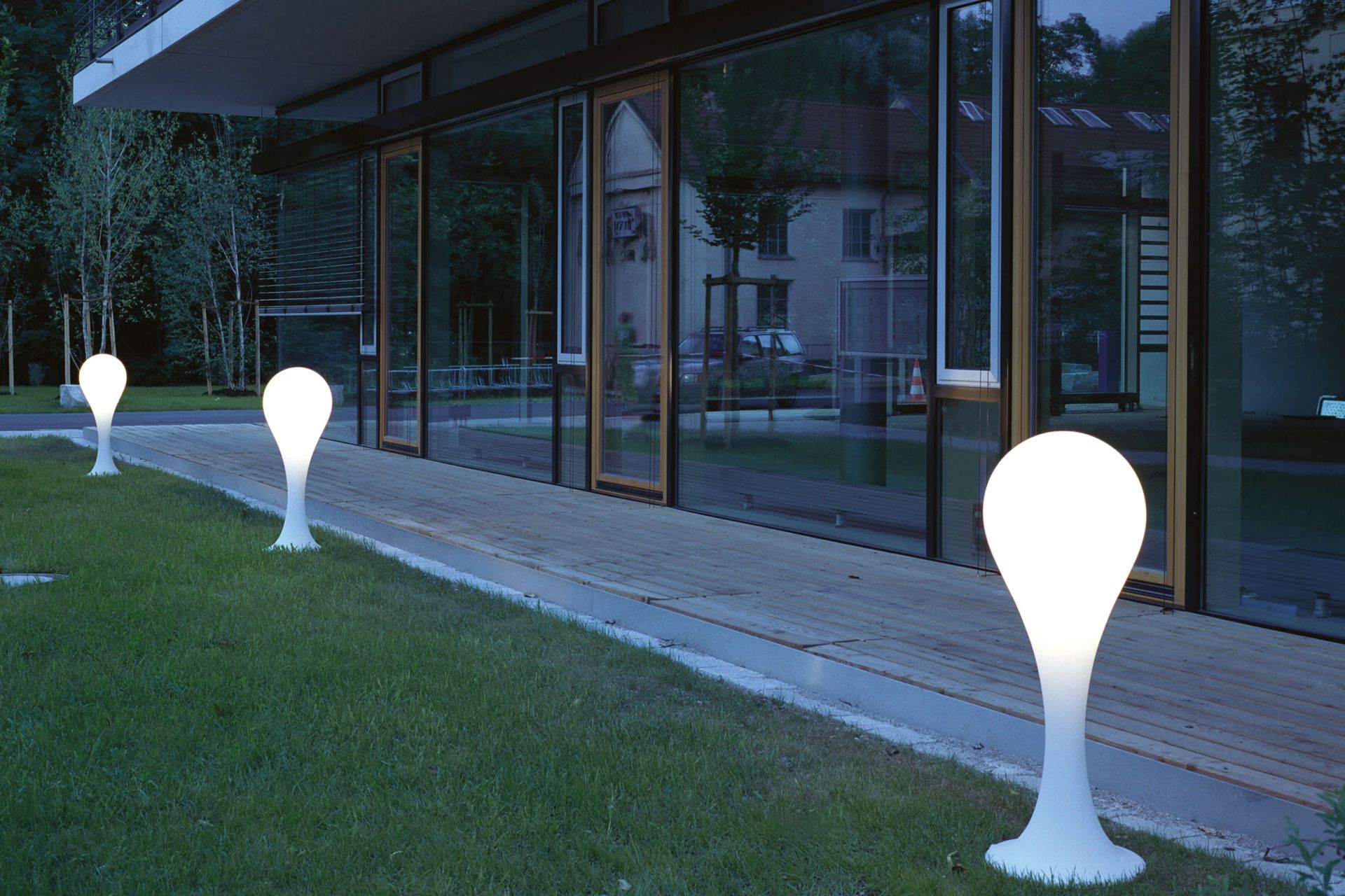 Drei Liquid Light Drop Outdoor Standleuchten von Next auf Rasen vor einem Gebäude.