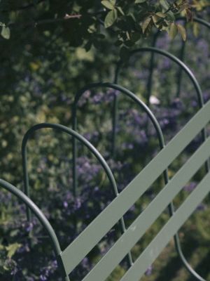 Detailaufnahme des Gardener's Sofa Outdoor von Design House Stockholm, grüne Metallstruktur vor blühendem Garten.