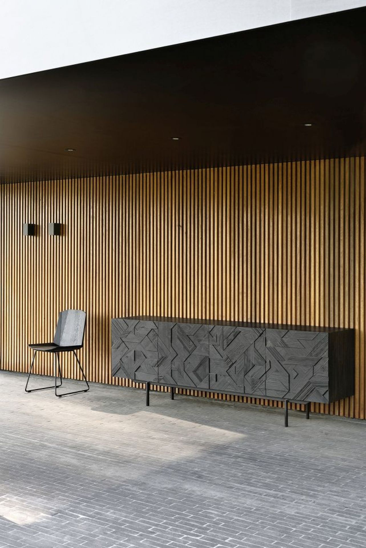 Schwarze Graphic Teak Anrichte von Ethnicraft mit geometrischem Muster und passendem Stuhl vor Holzpaneelwand.