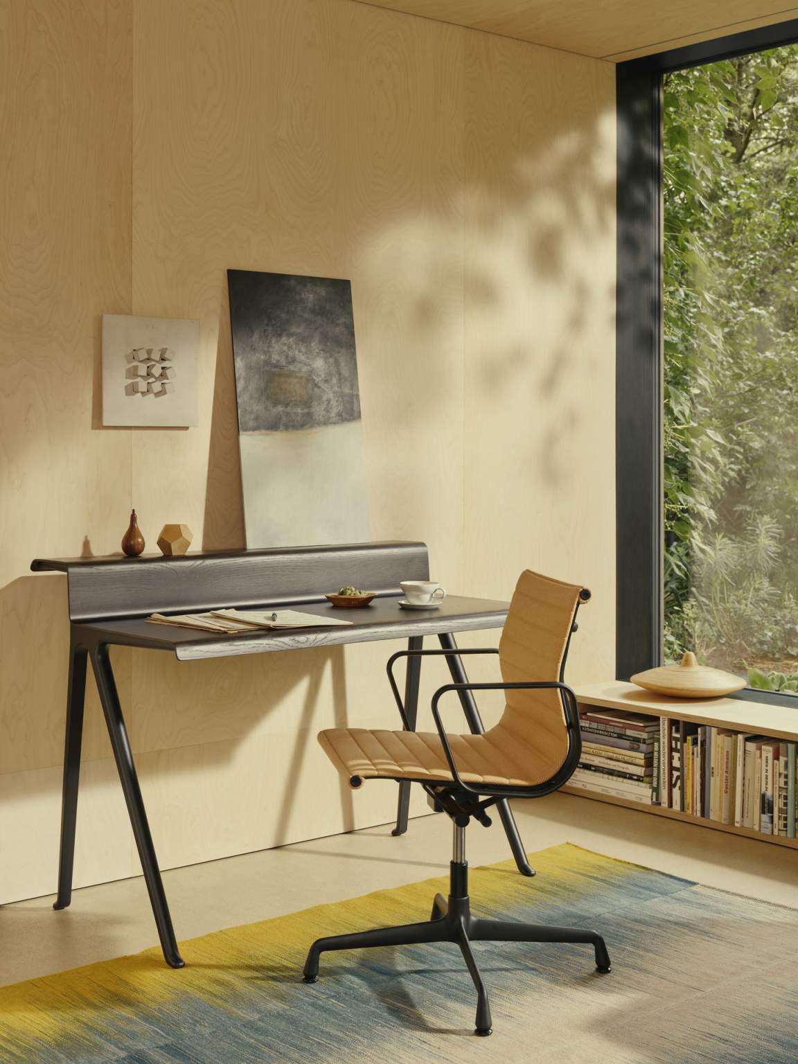 Vitra Courier Schreibtisch mit Bürostuhl in einem hellen Raum mit Bücherregal am Fenster.