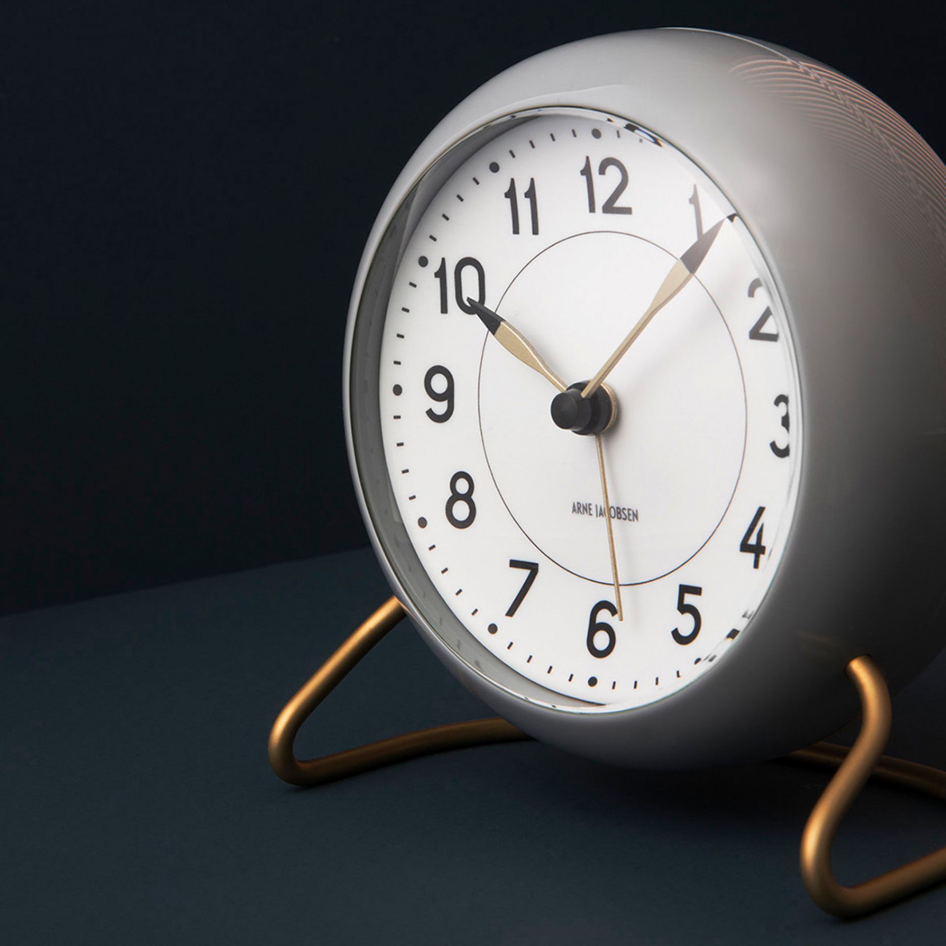 Grau-weisse Arne Jacobsen Station Tischuhr von Rosendahl Timepieces mit goldenem Standfuß. Design-Klassiker für Nachttisch und Büro.